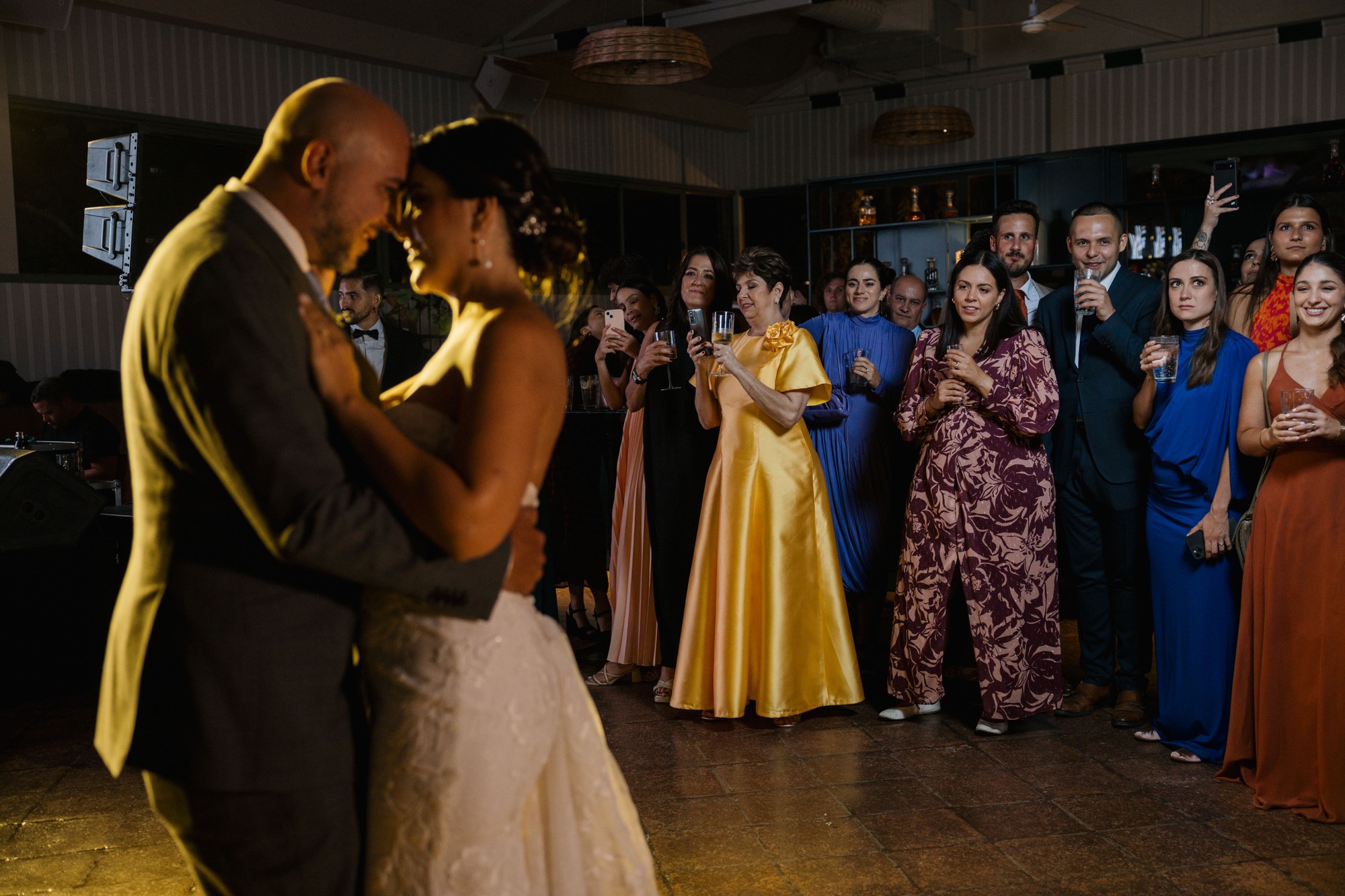 Los invitados observan el primer baile de los novios copa en mano