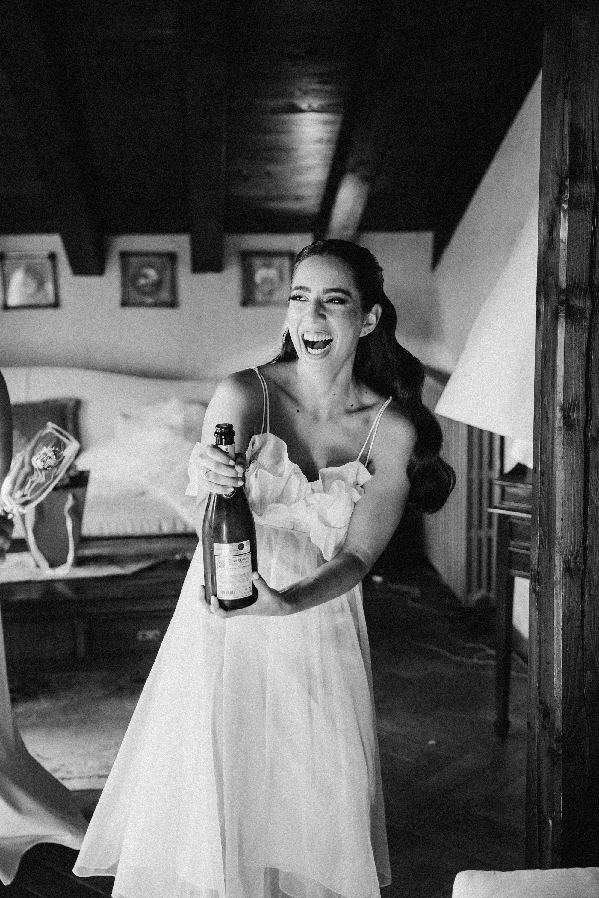 La novia estalla de risa con la botella de champán en la mano durante los preparativos