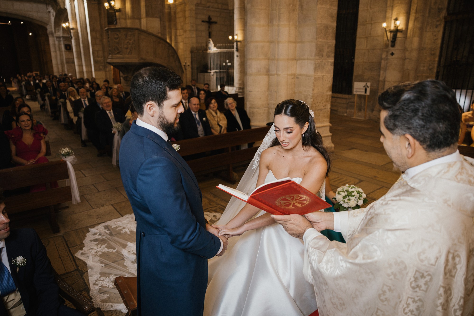 El sacerdote sostiene el libro abierto mientras los novios se dan la mano ante el altar