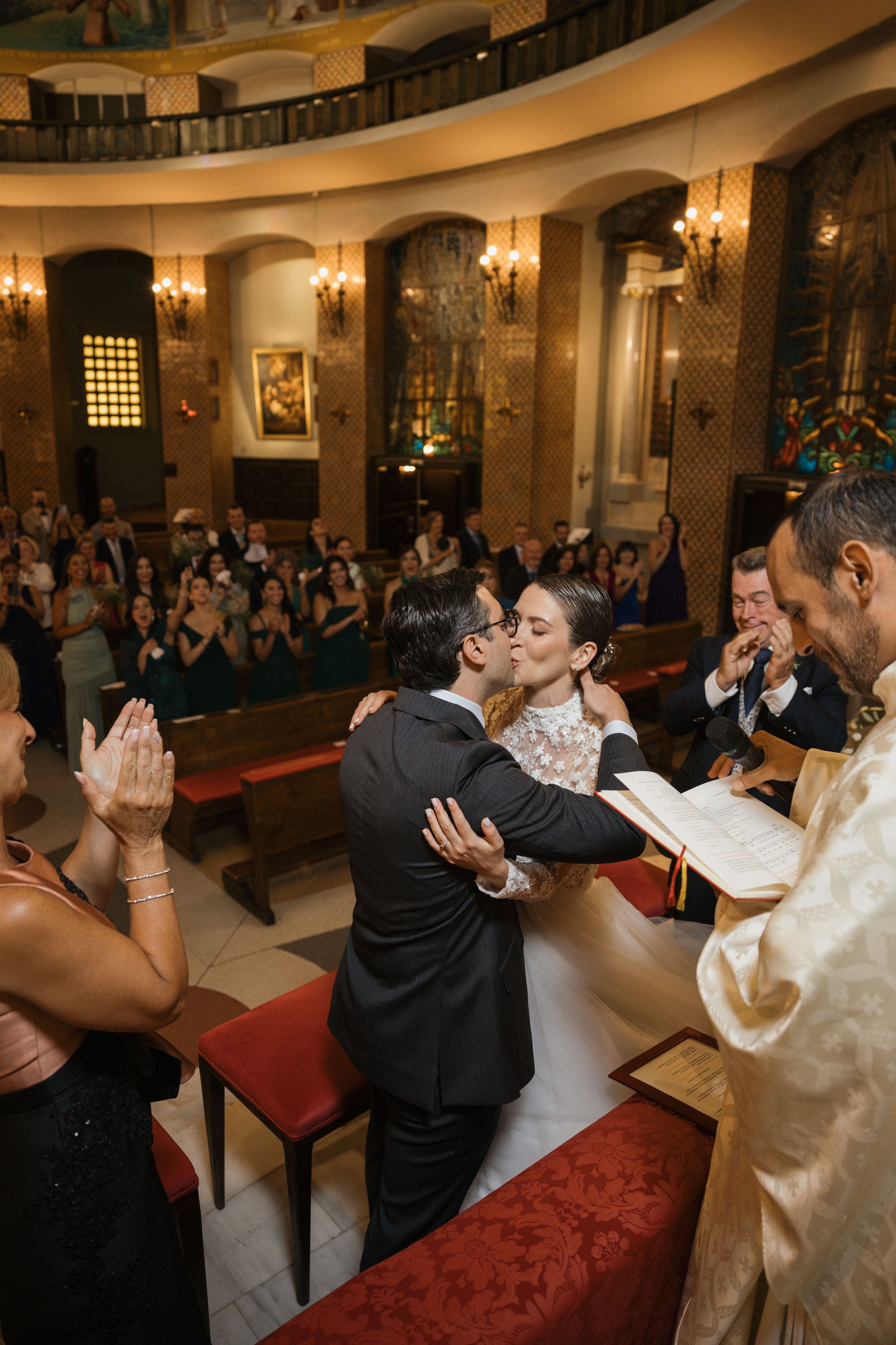 Los novios se besan ante el altar mientras los invitados aplauden