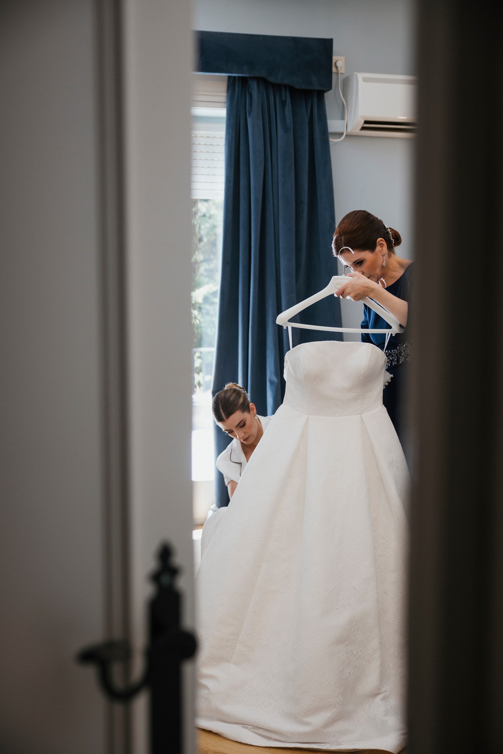 Dos invitadas preparan el vestido de novia, vistas a través del quicio de la puerta