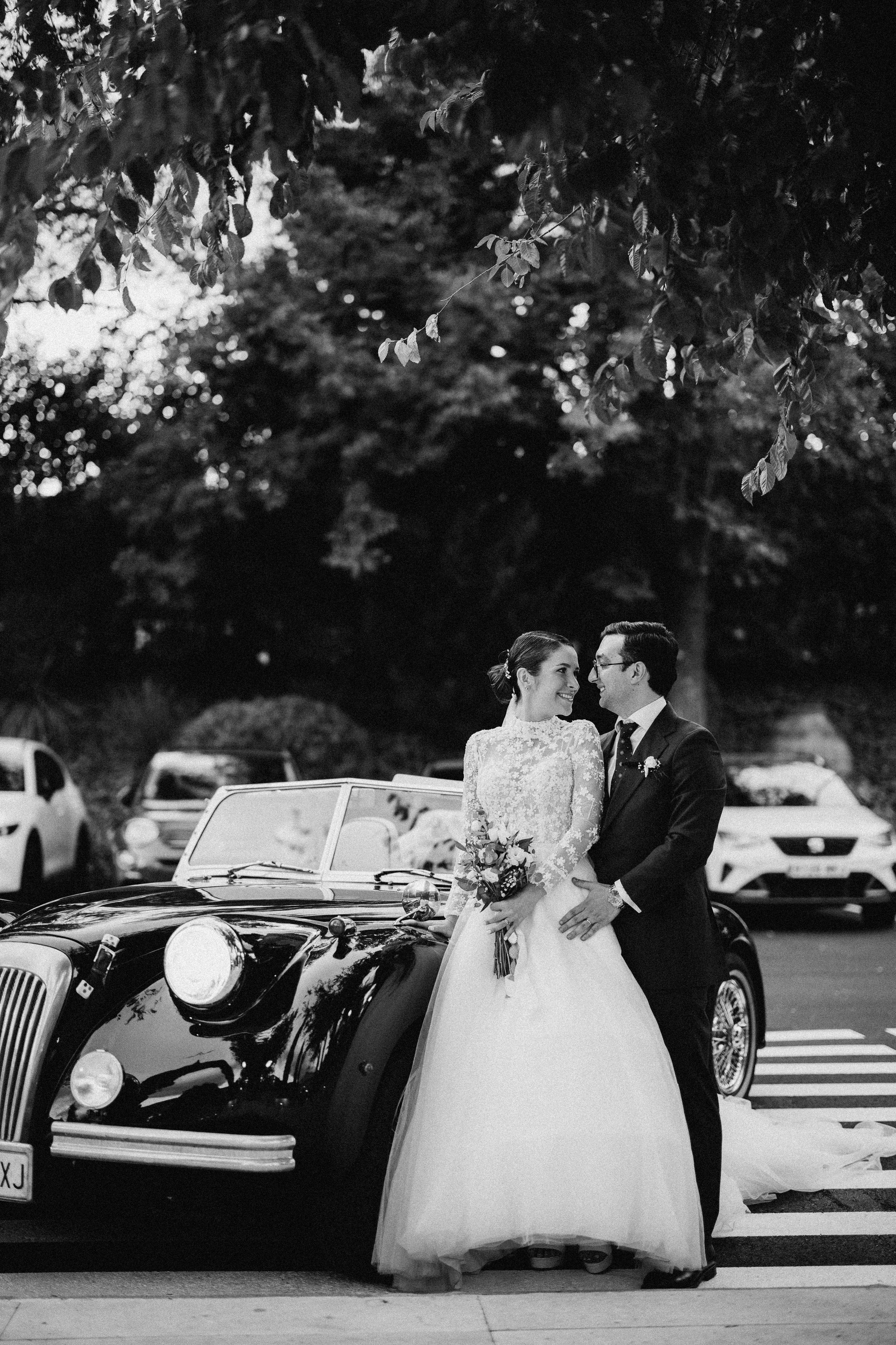 Los novios posan apoyados en un descapotable clásico, en blanco y negro