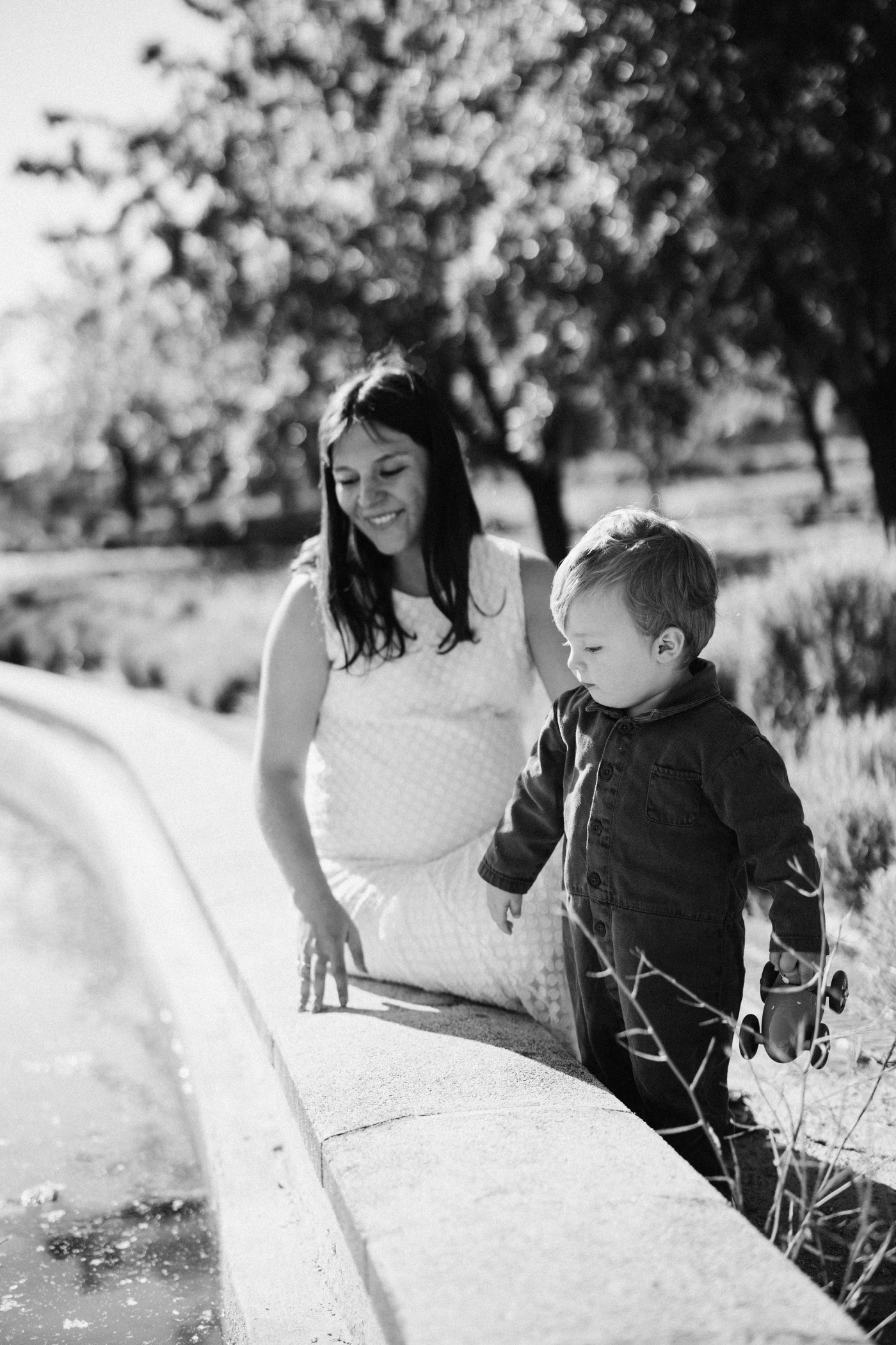 Madre embarazada sonriendo a su hijo junto a una fuente