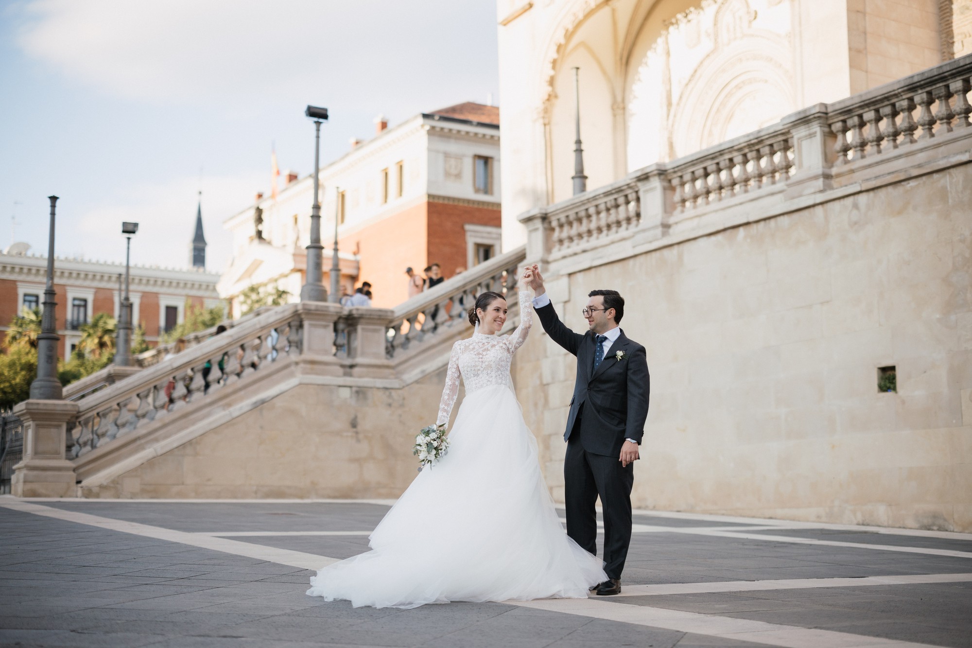El novio hace girar a la novia sobre el empedrado junto a una gran escalinata de piedra