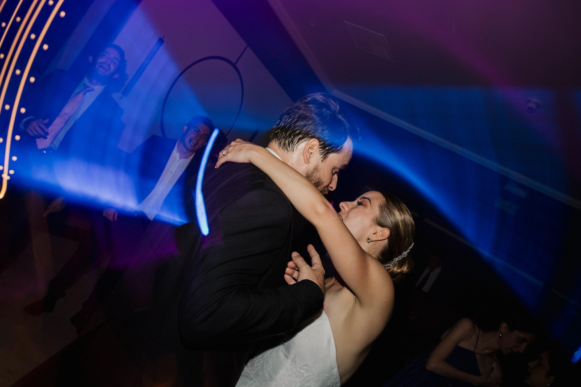 Los novios se besan en la pista entre las luces azules de la fiesta