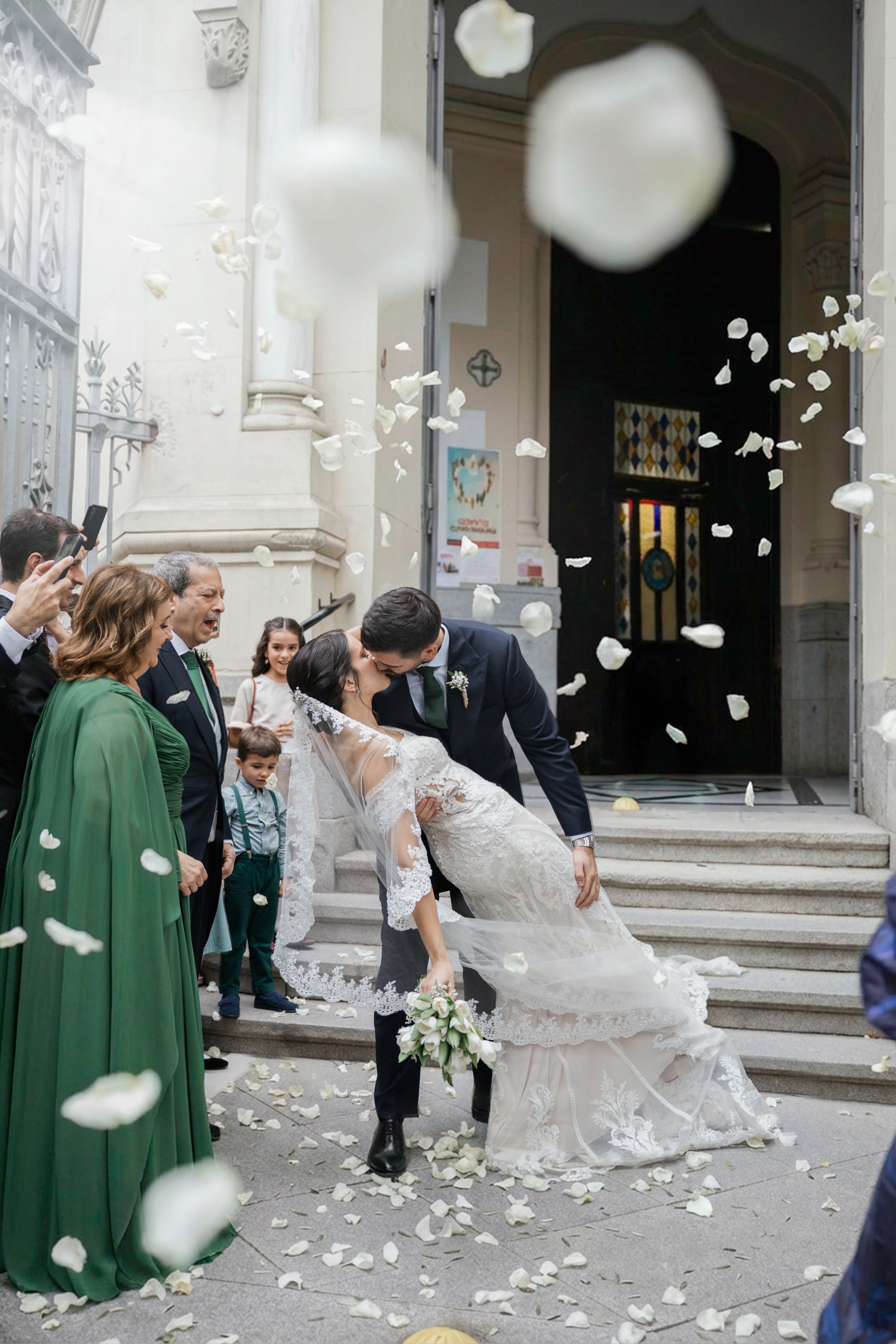 Los novios se besan a la salida de la iglesia bajo una lluvia de pétalos blancos