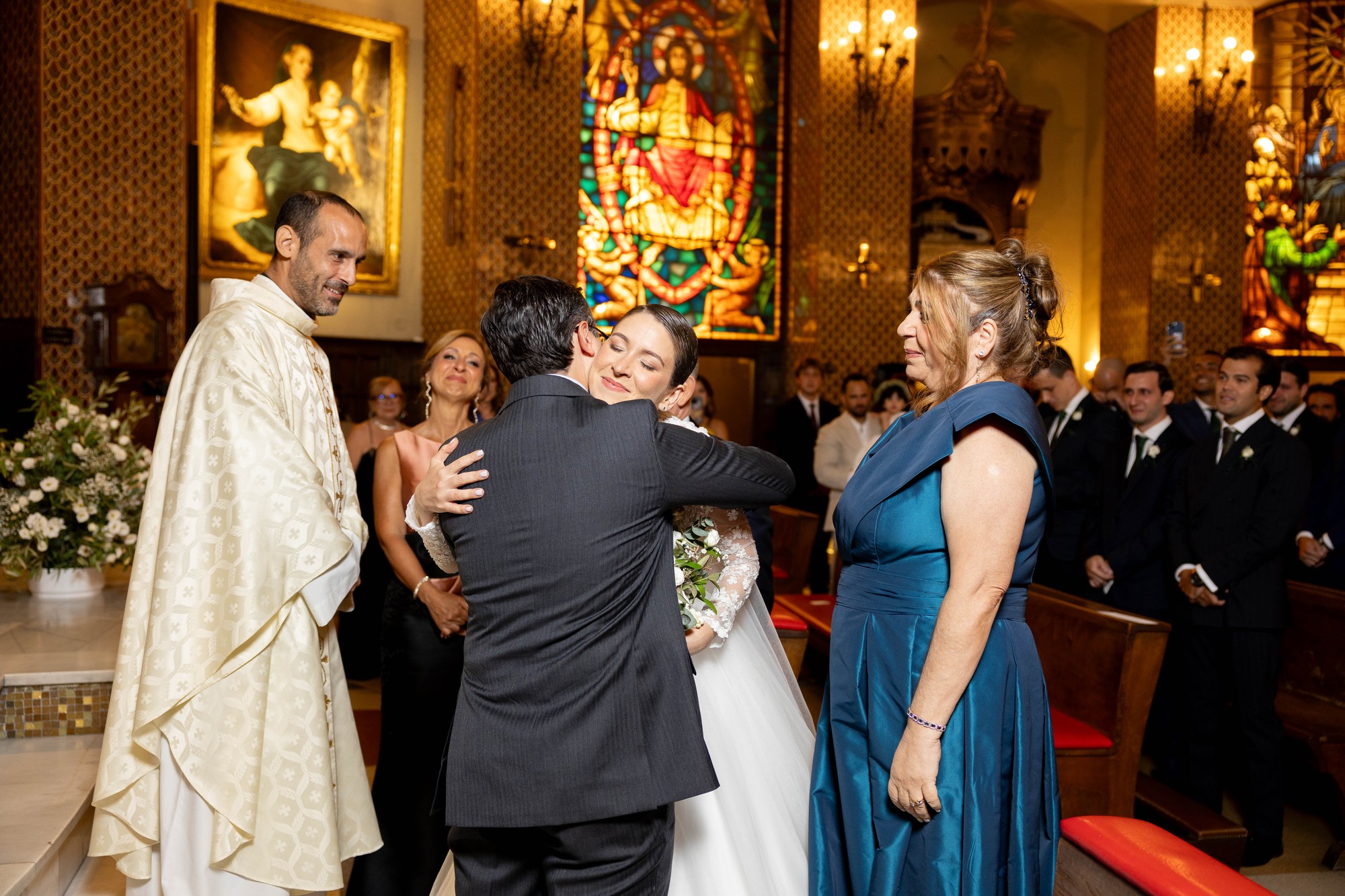 El novio abraza a la novia al pie del altar bajo la mirada del sacerdote