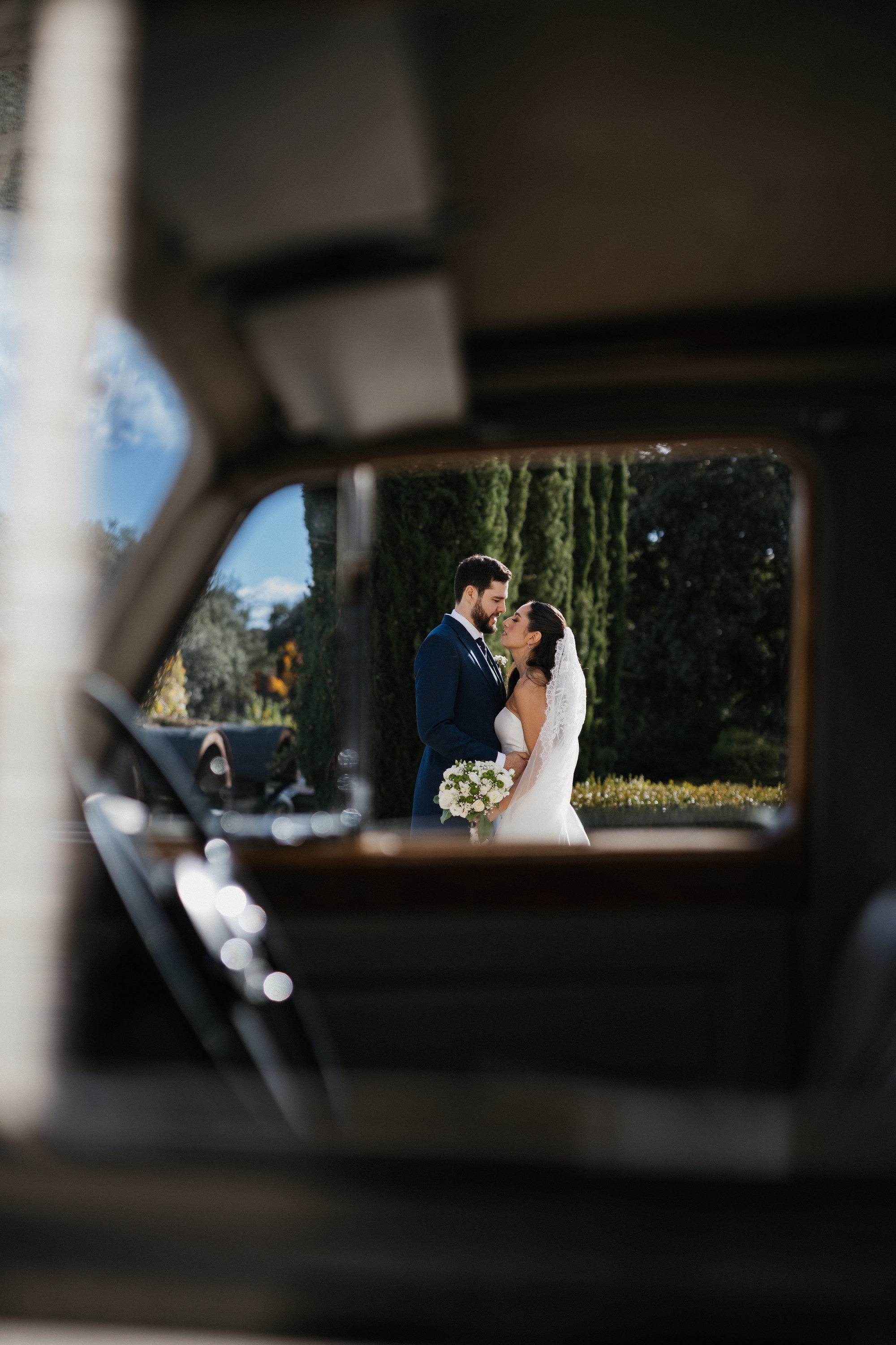 Los novios se miran de cerca, enmarcados por la ventanilla abierta del coche clásico