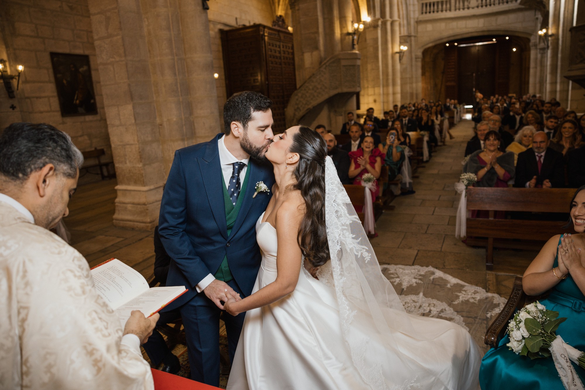 Los novios se besan ante el altar mientras los invitados aplauden desde los bancos