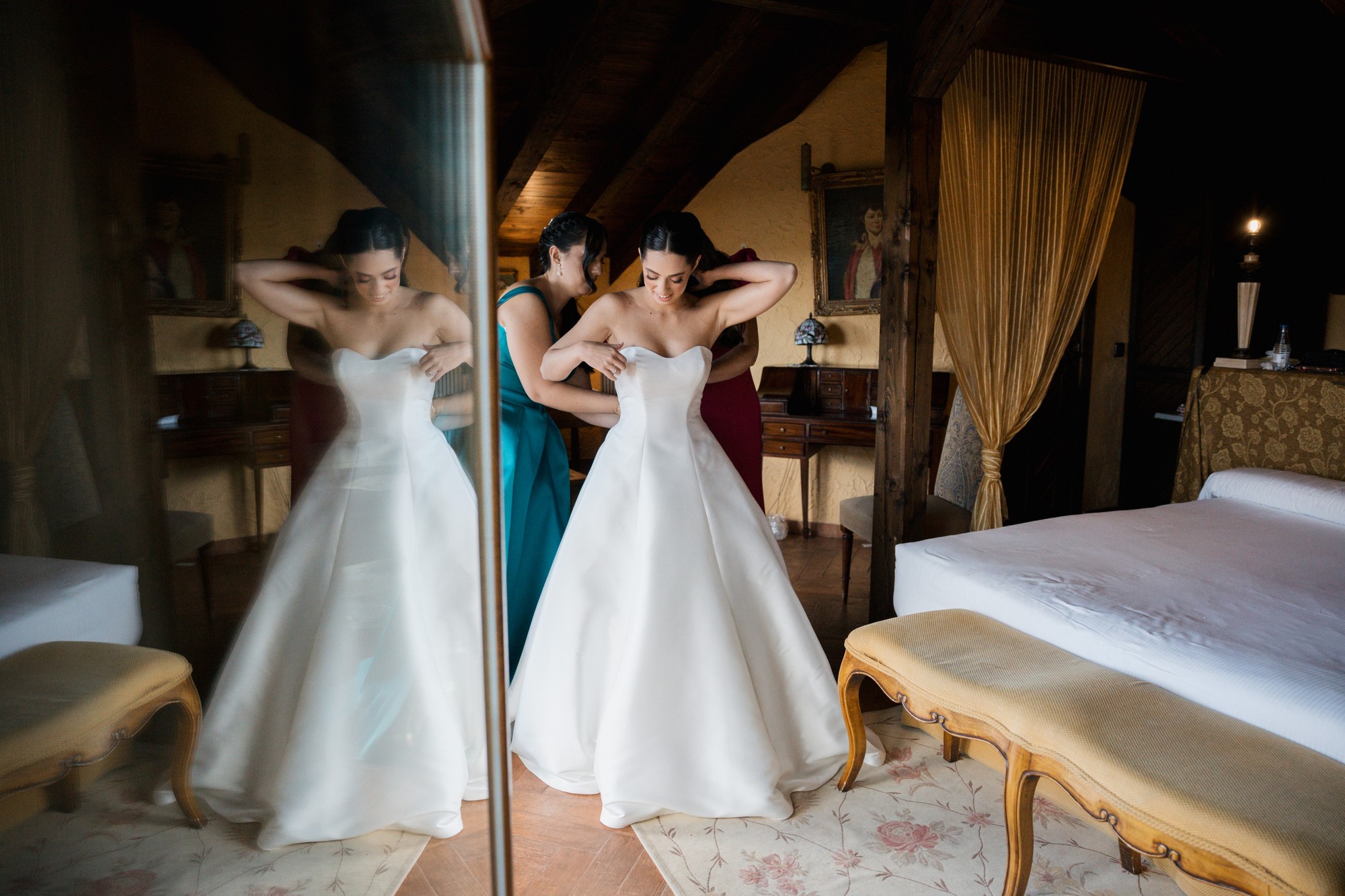 Abrochan el vestido de la novia frente al espejo del dormitorio y el reflejo duplica la escena