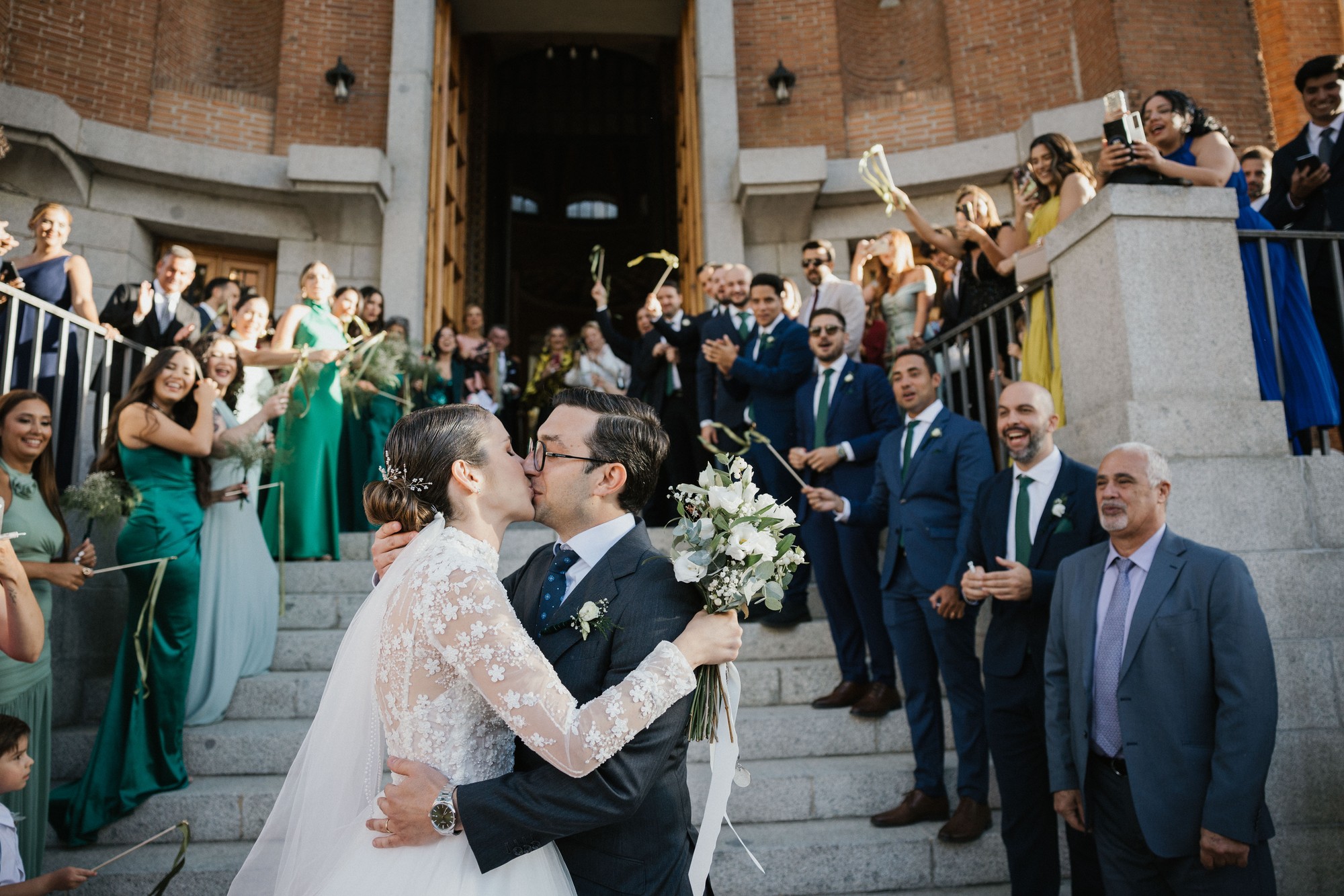 Los recién casados se besan en la escalinata de la iglesia rodeados de invitados