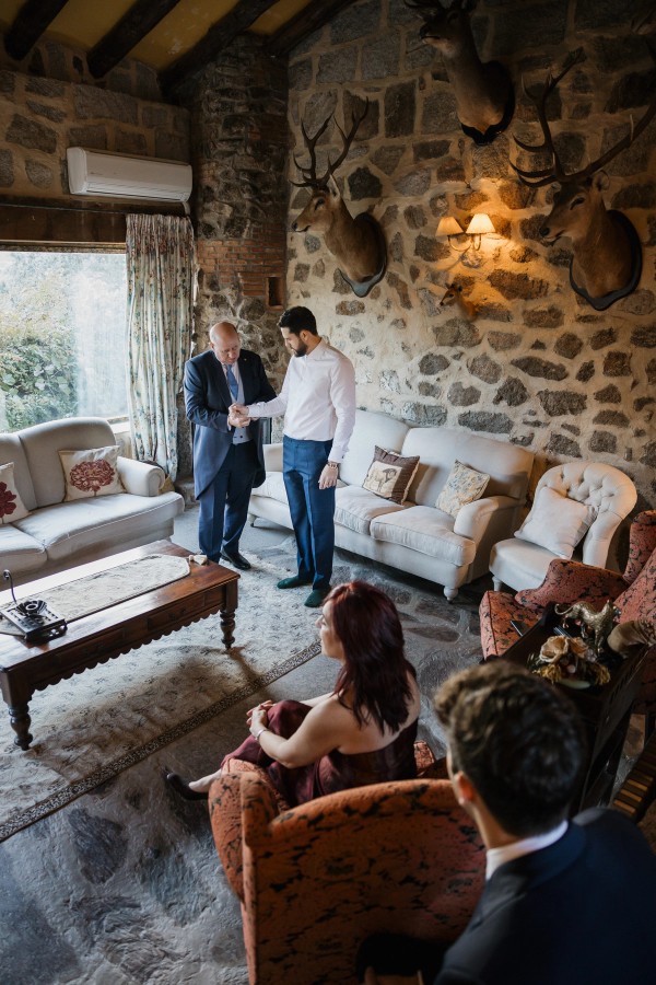 A guest helps the groom with his shirt cuffs in the estate's sitting room