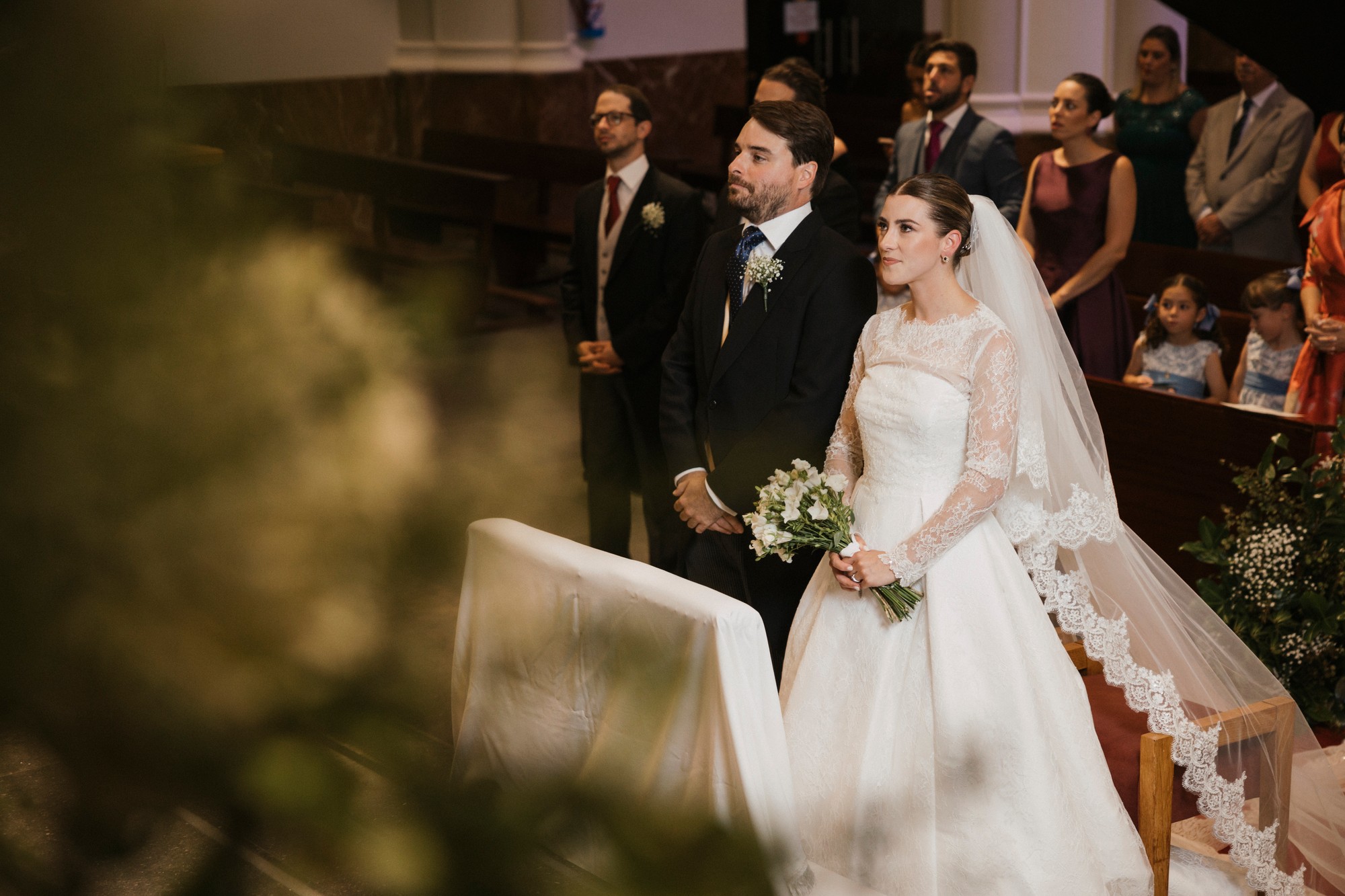 Los novios de pie ante el altar, vistos entre las flores de la ceremonia