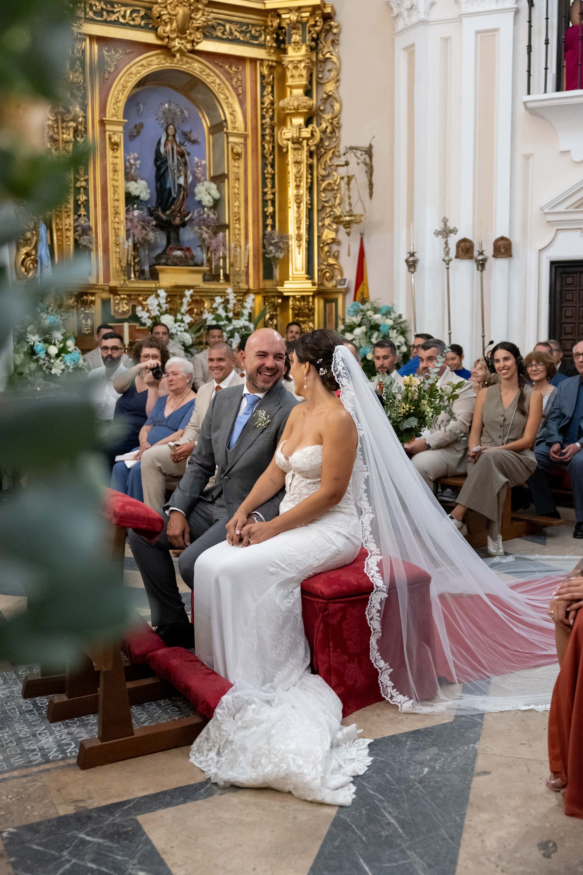 Los novios se ríen sentados durante la ceremonia con el velo desplegado a su lado