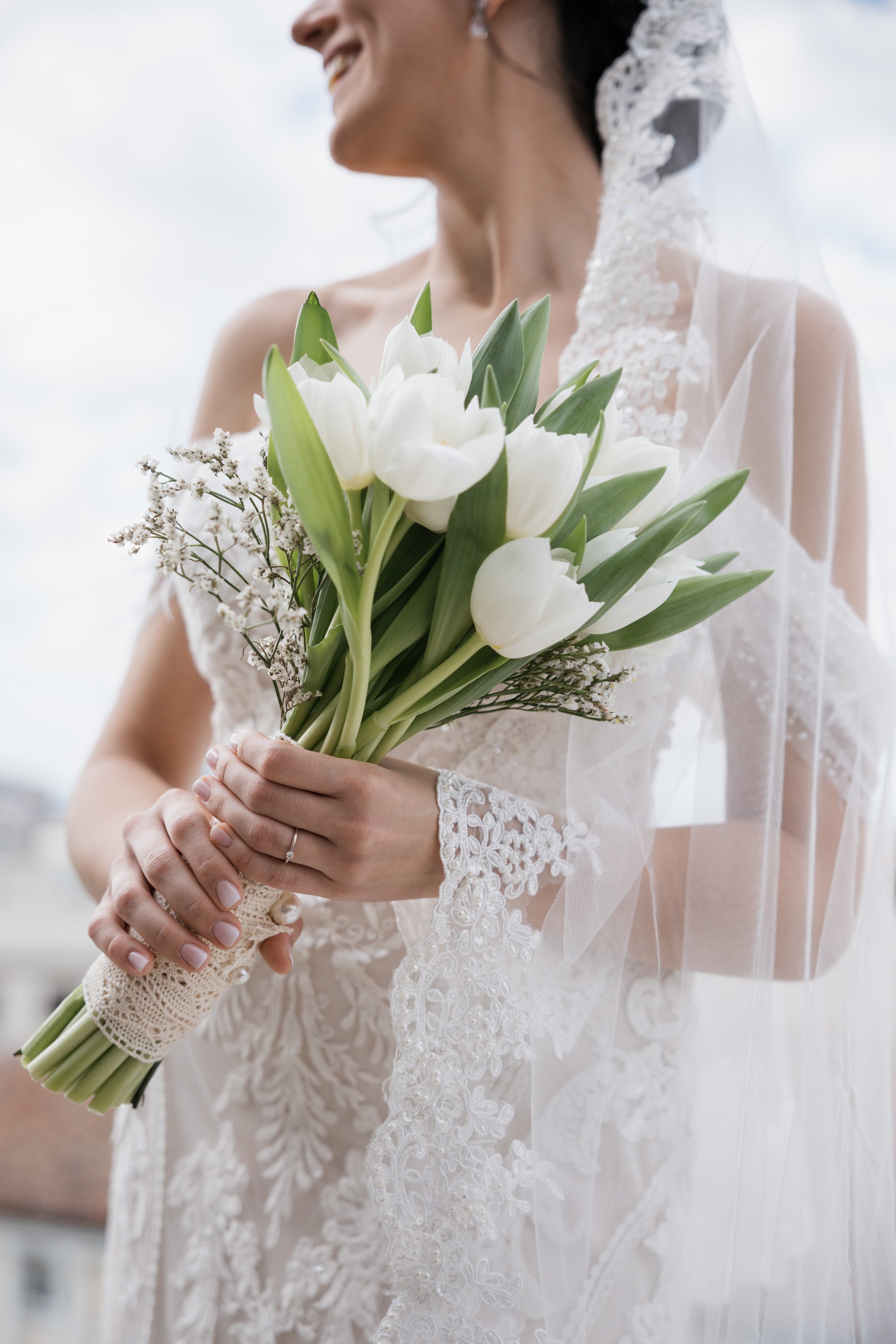 Las manos de la novia sostienen el ramo de tulipanes blancos envuelto en encaje