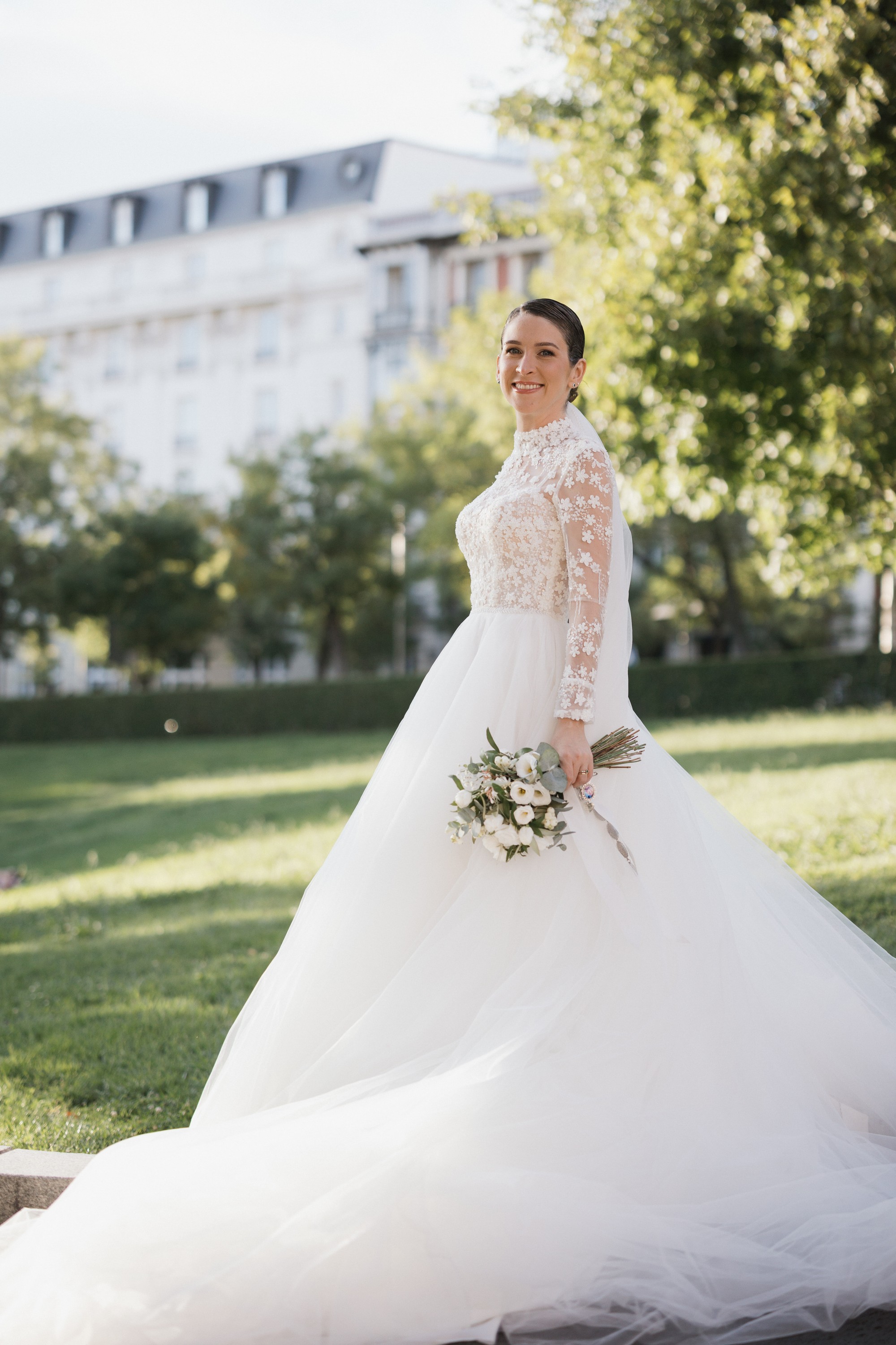 La novia posa sobre el césped con la cola de tul desplegada a su alrededor