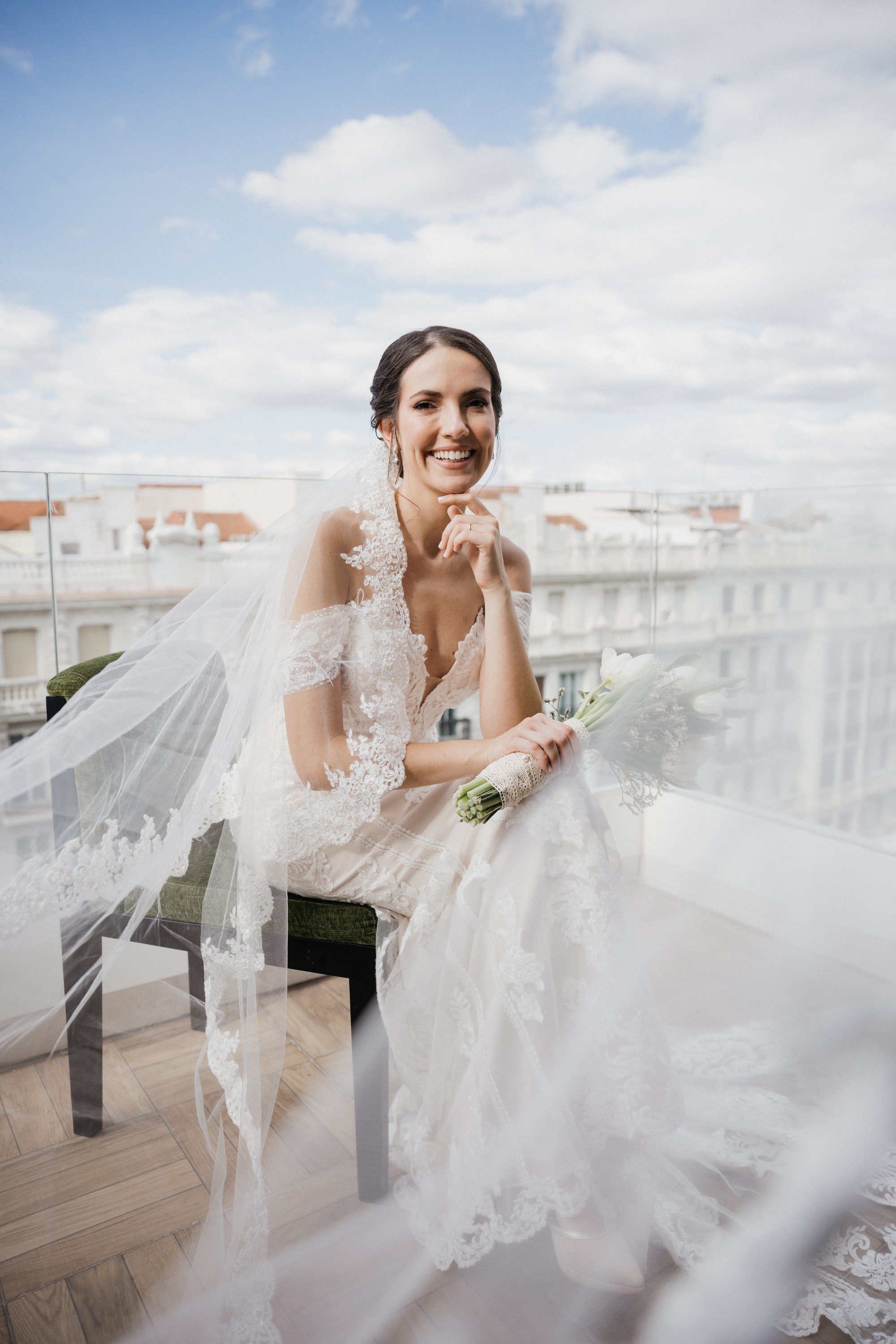 La novia ríe sentada en la terraza mientras el velo vuela a su alrededor