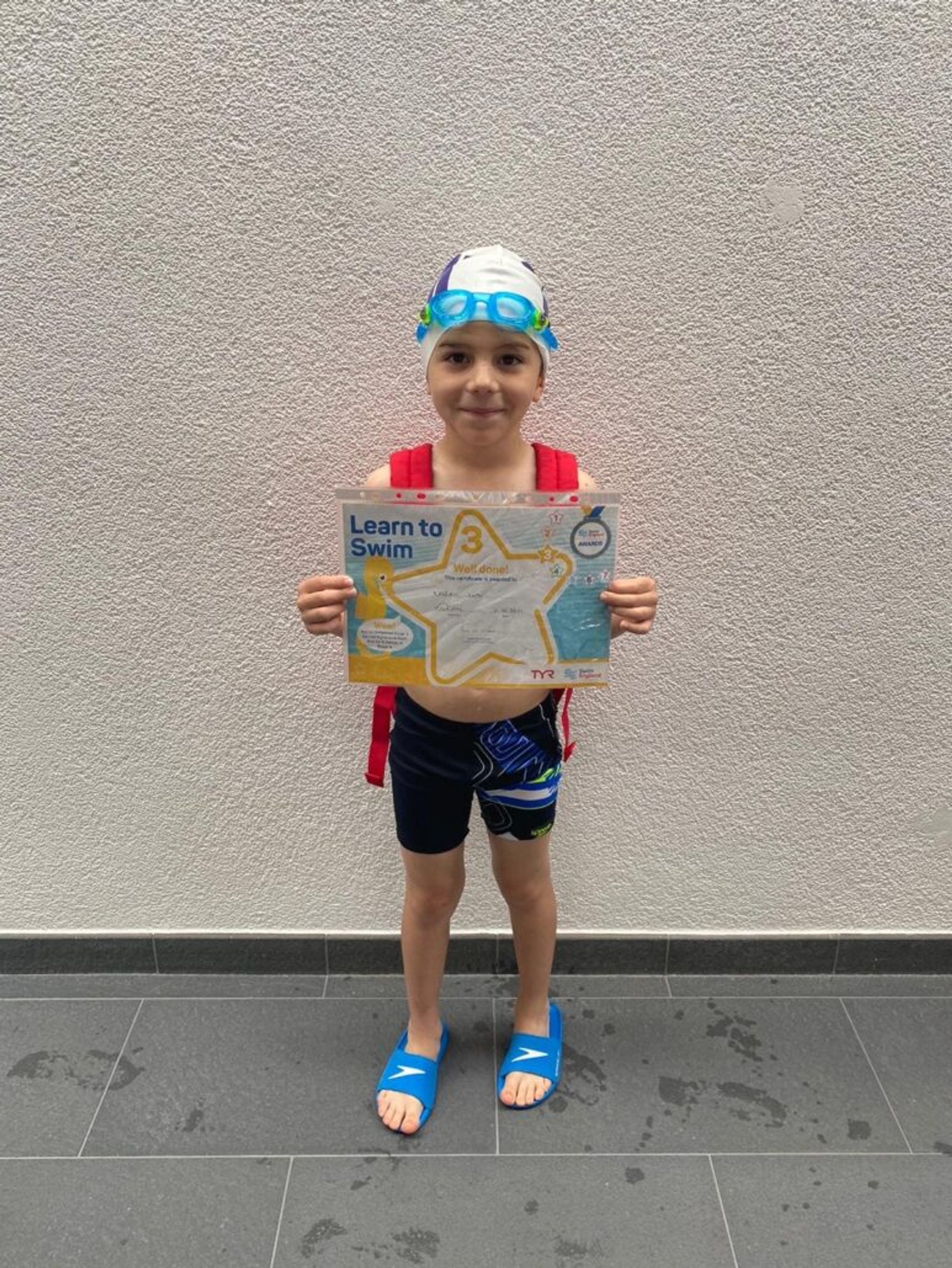 A young swimmer proudly holding a Learn to Swim certificate