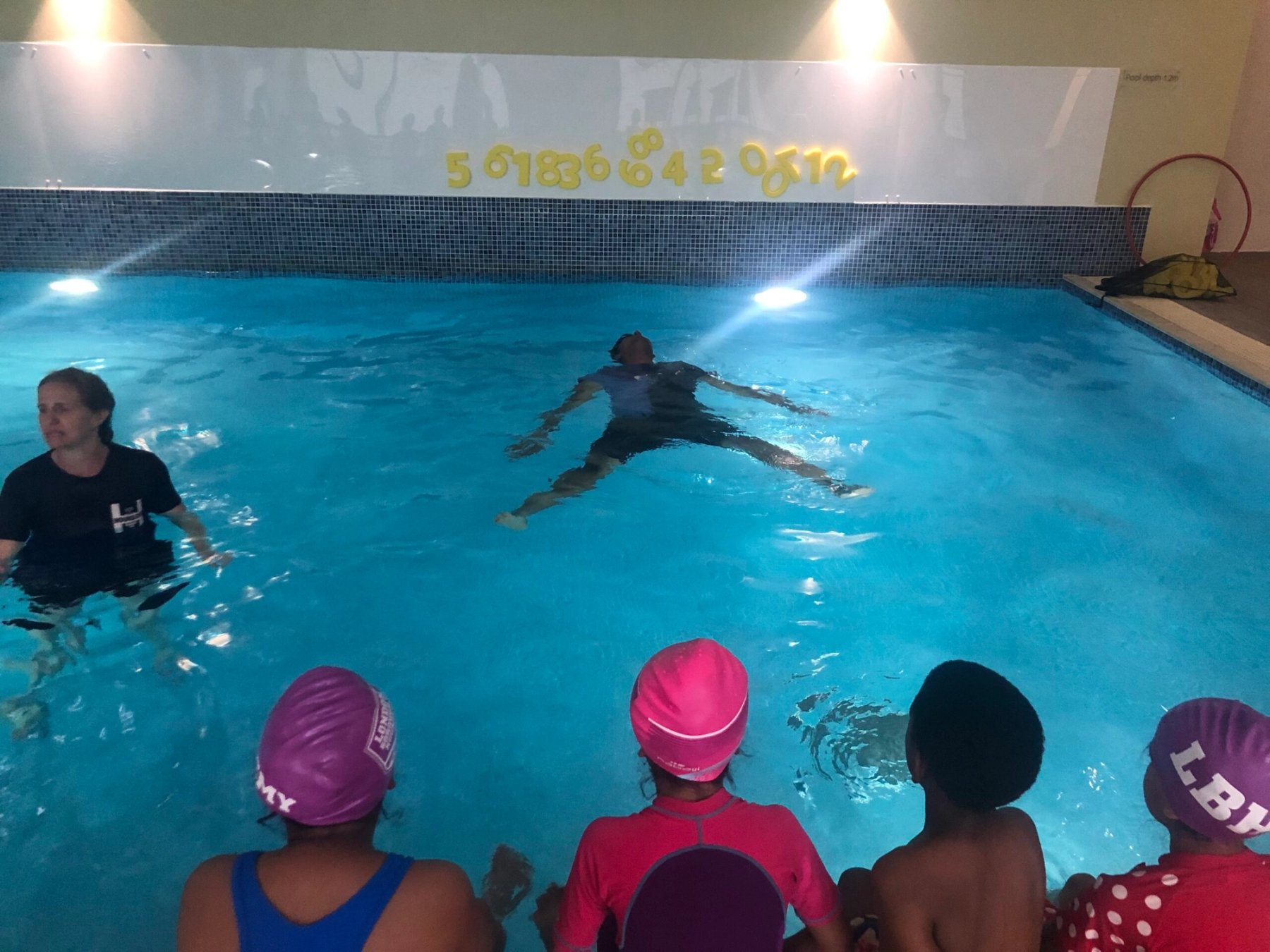 Swimmers in club caps watching a demonstration from the poolside