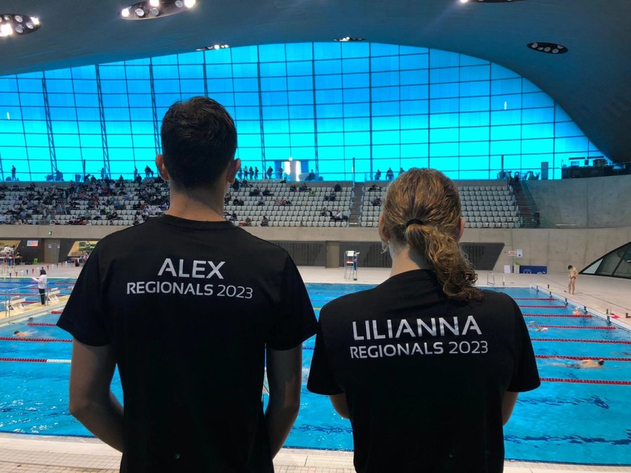 Two LBHSC swimmers in Regionals 2023 shirts looking out over the pool at the London Aquatics Centre