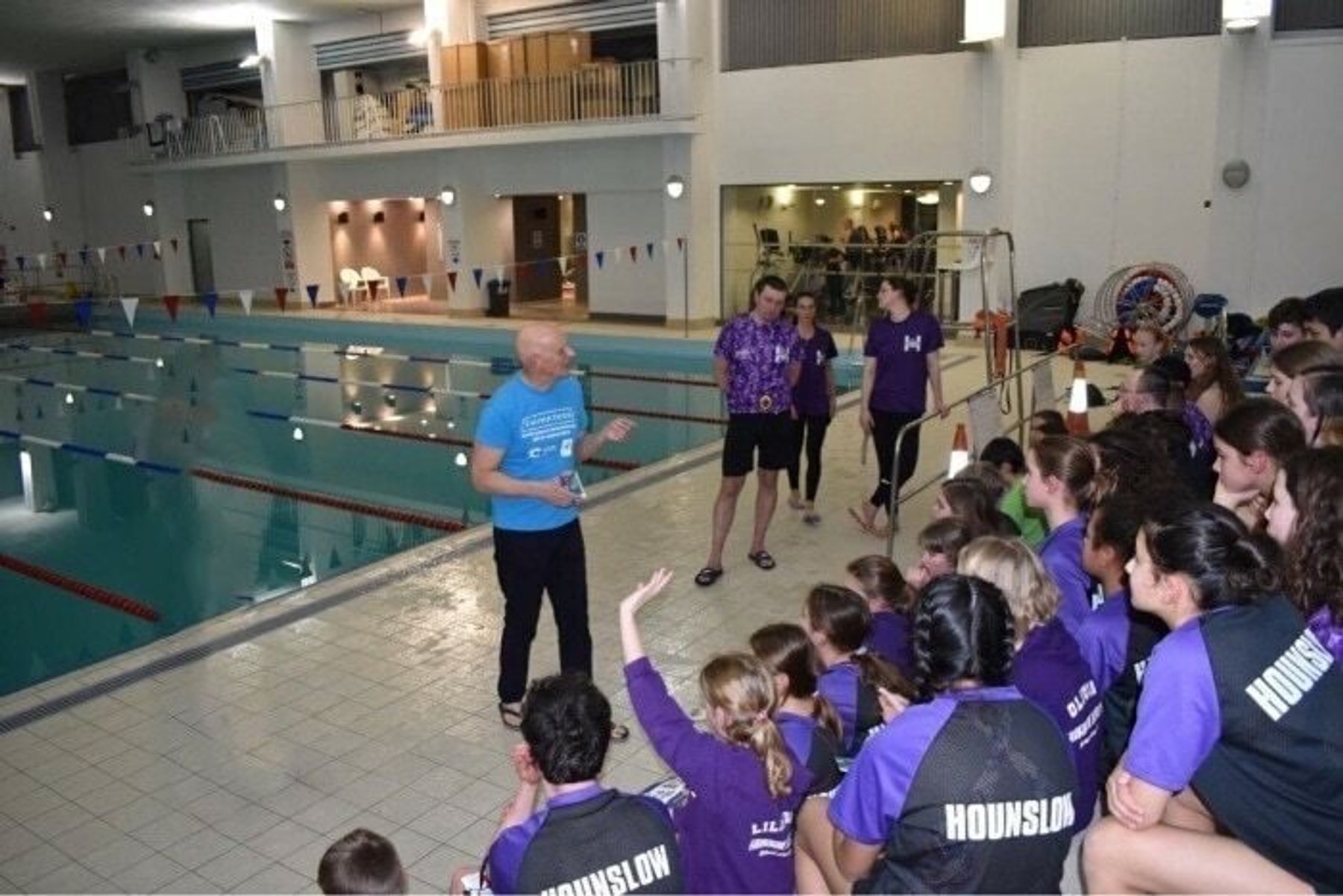 A coach briefing squad swimmers poolside before a session