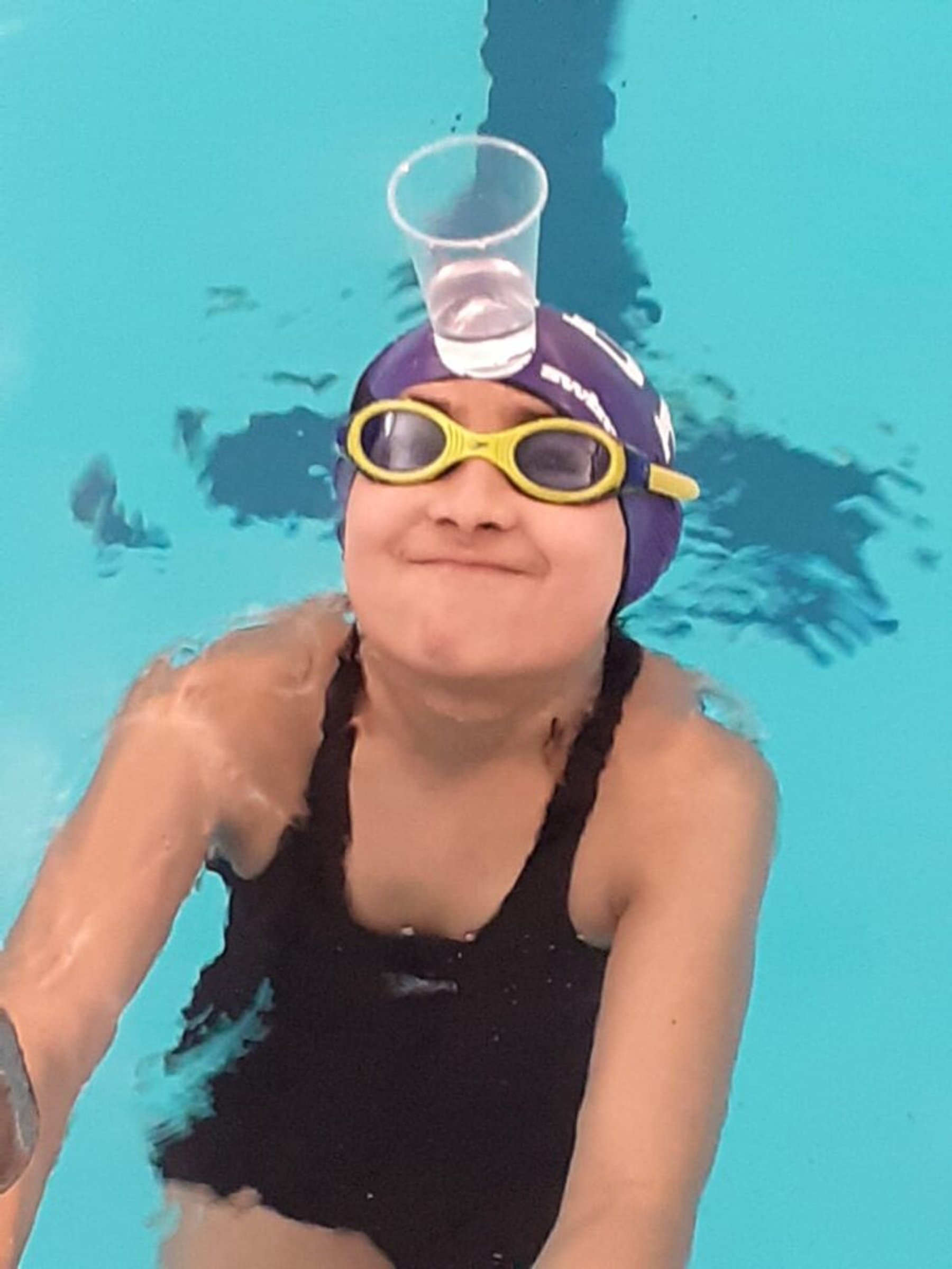 A young swimmer balancing a cup on her swim cap in the water
