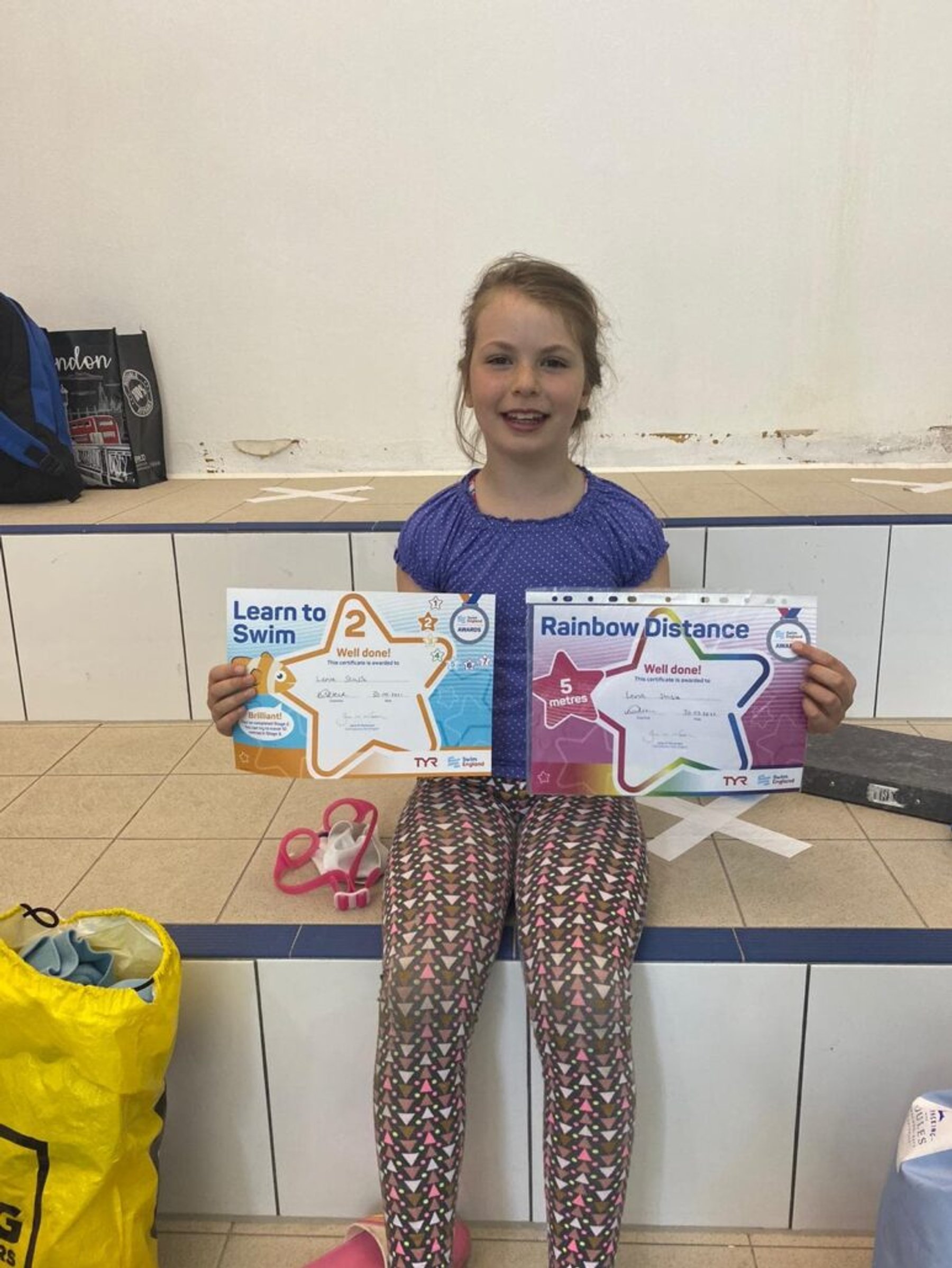 A young swimmer showing two Learn to Swim certificates