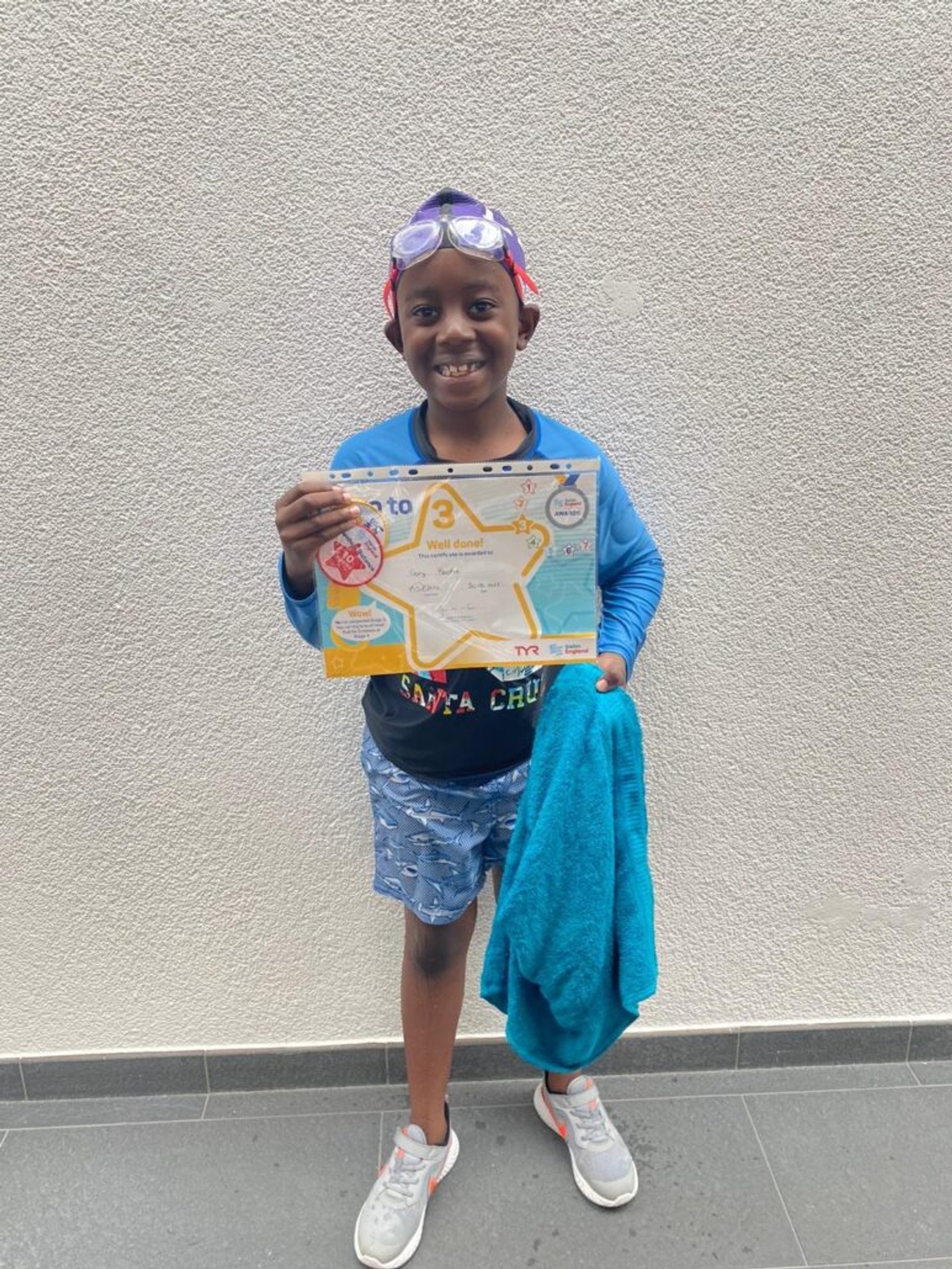 A young swimmer holding a Learn to Swim certificate after a lesson
