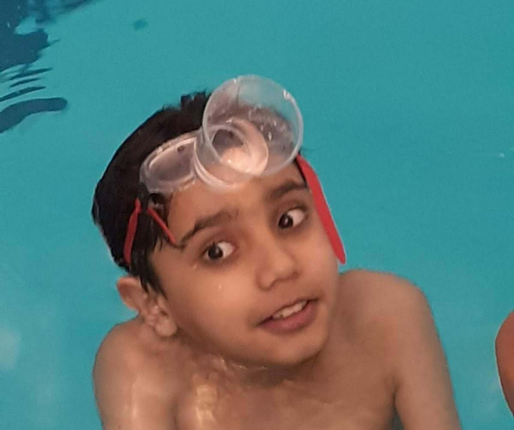 A young swimmer grinning in the water with goggles on his forehead