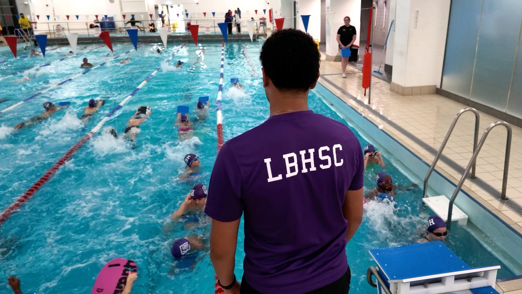 An LBHSC coach watching swimmers train with kickboards across the lanes at Isleworth Pool