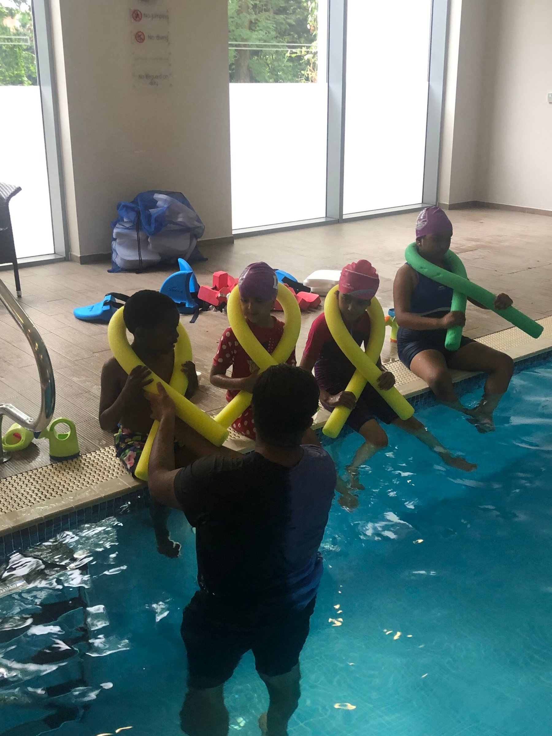 An instructor supporting swimmers with noodles at the pool steps