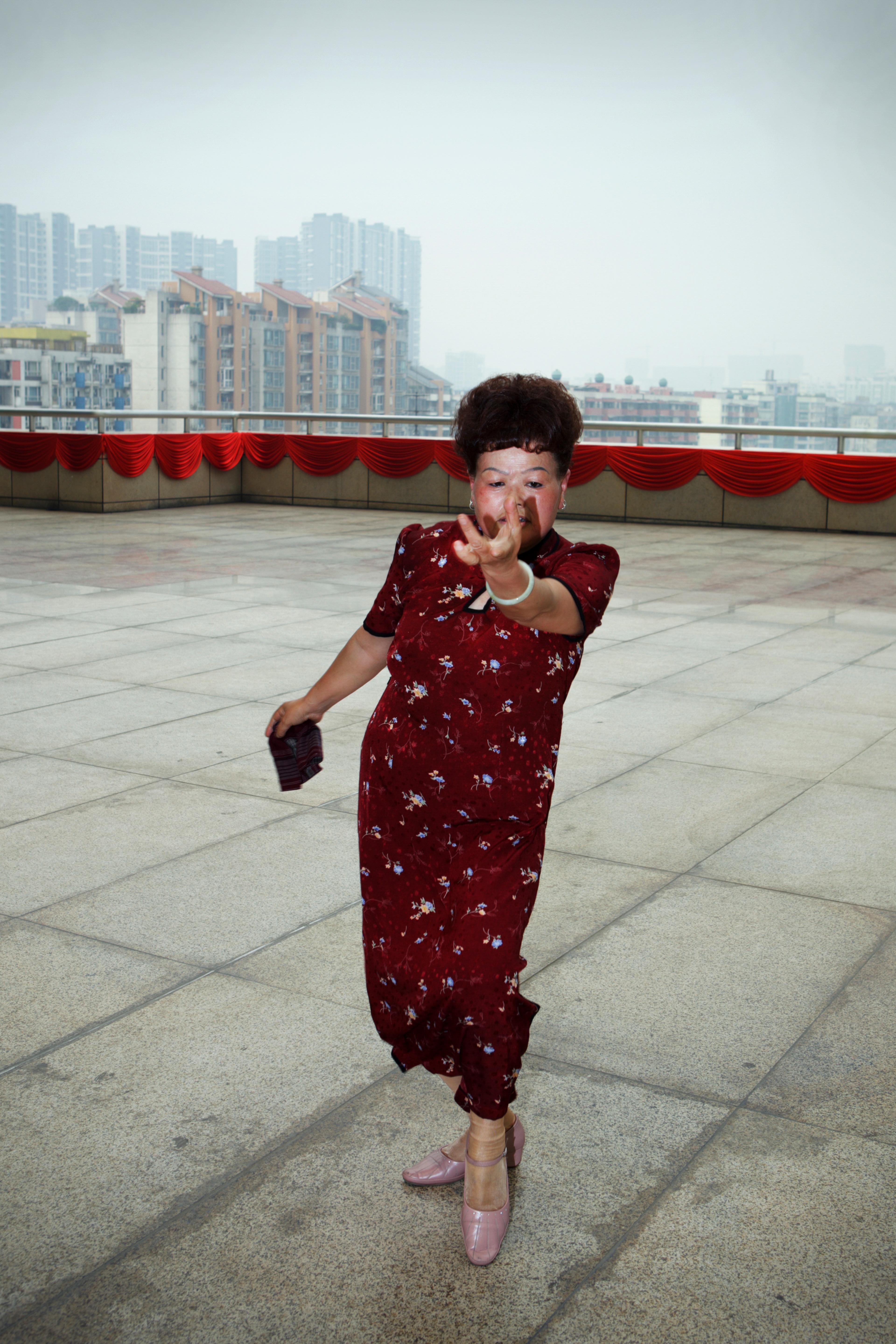 Women in a red dress captured on a wide terrace with large buildings in the background