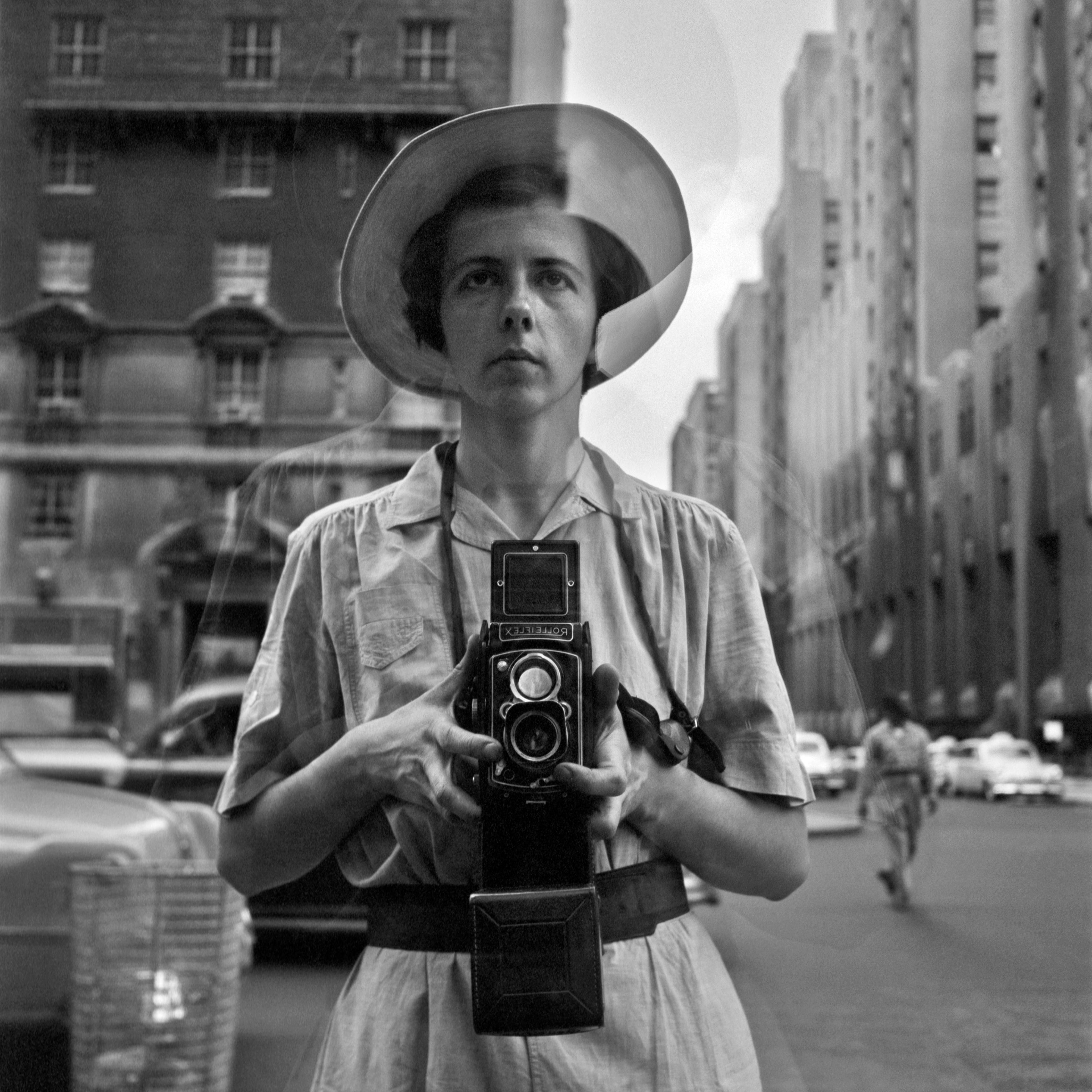 A black-and-white photograph of a woman's reflection in a store window in an urban setting