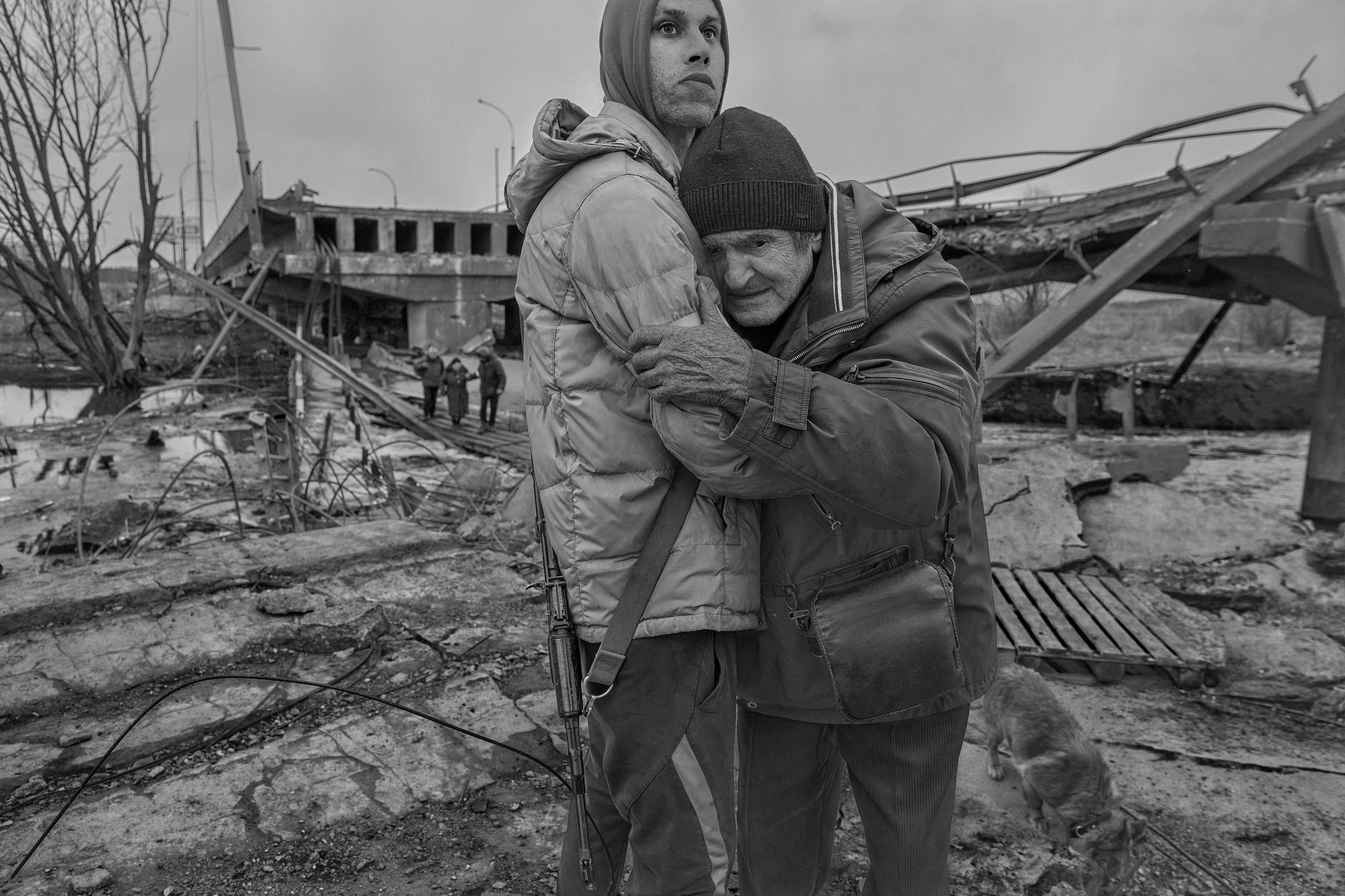 Black and white image of two men holding each other in front of a destroyed surrounding