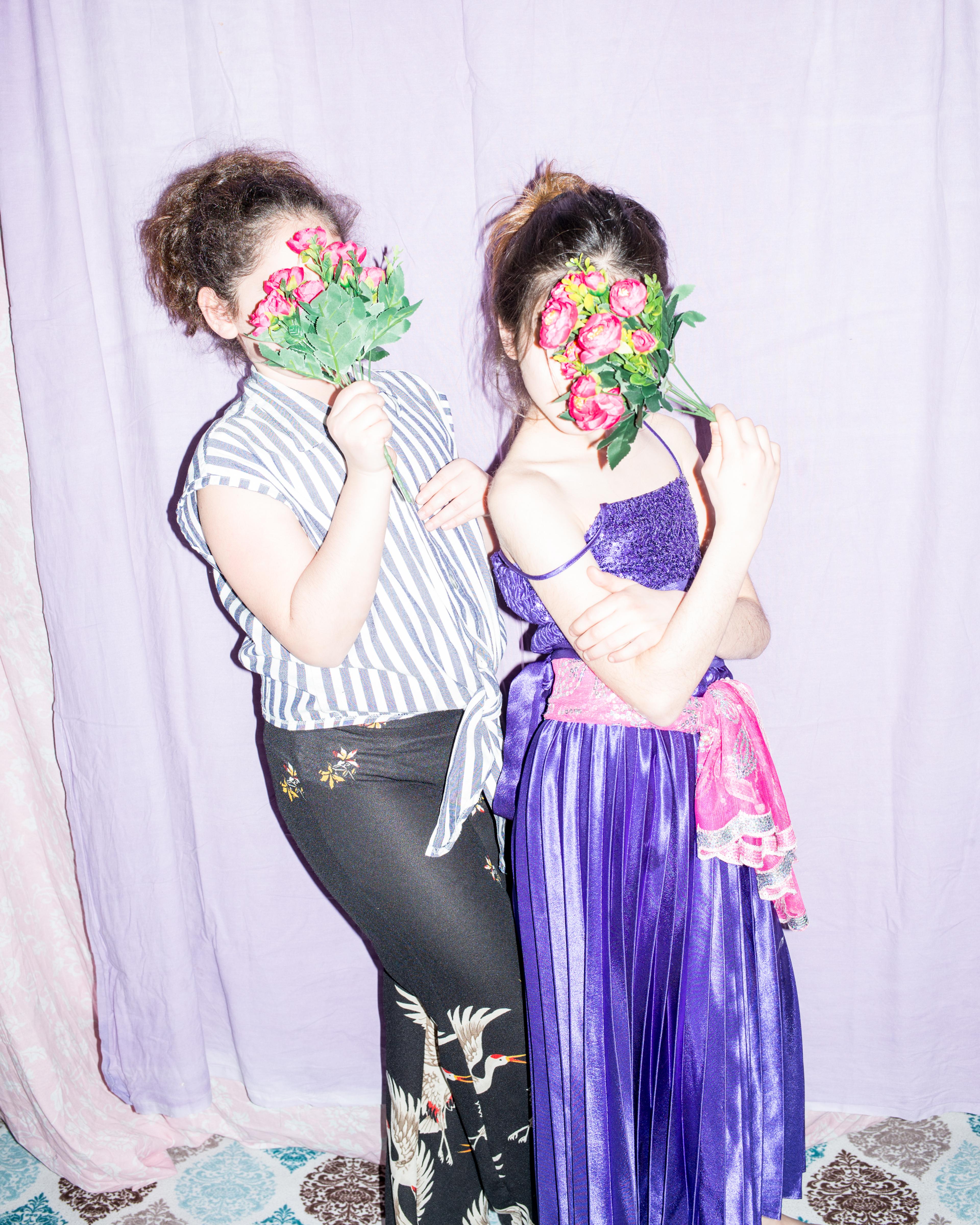 Flash photography image of two girls holding a small bouquet of flowers in front of their faces