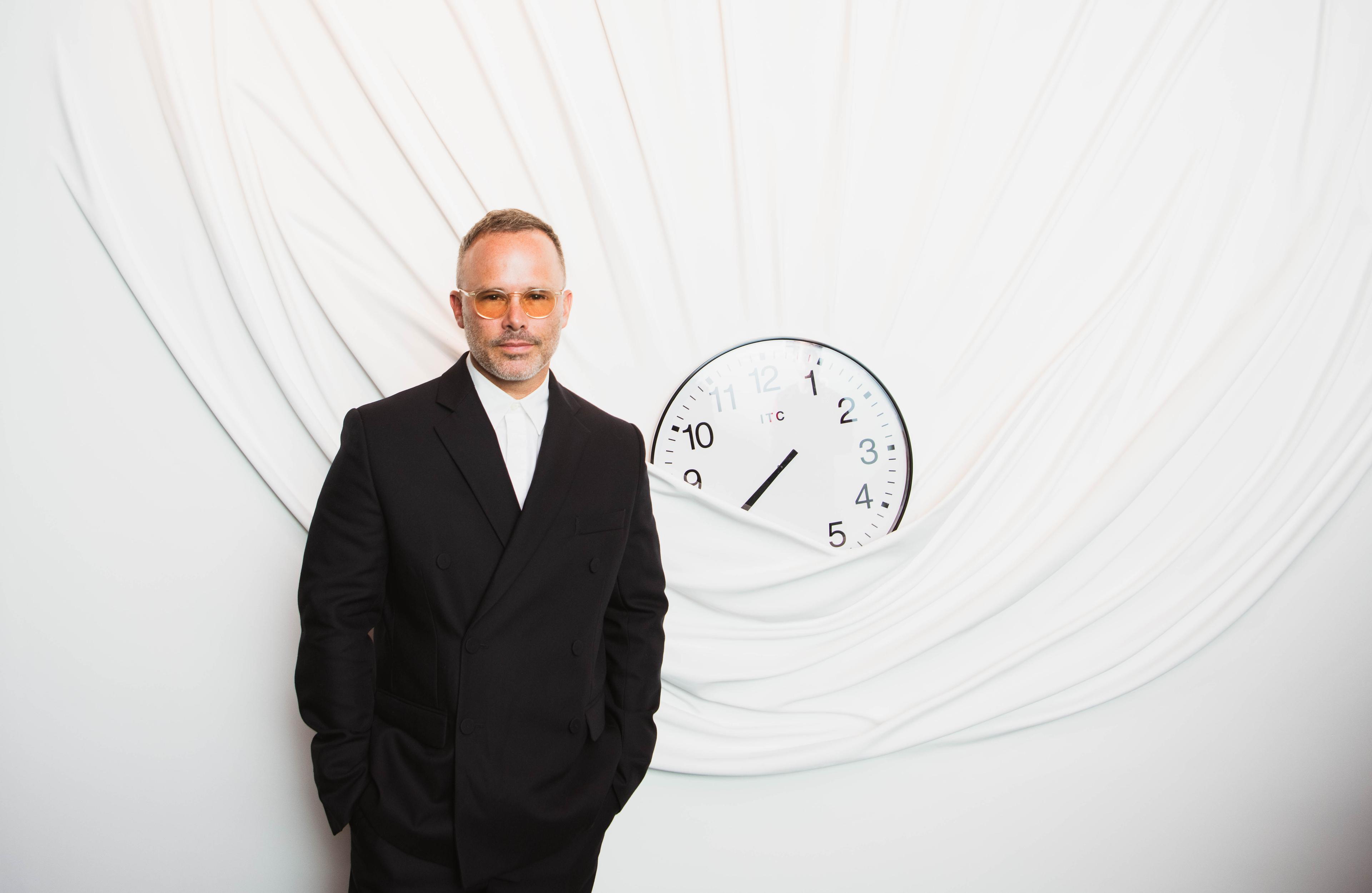Portrait of Daniel Arsham next to a wall sculpture of a clock draped in fabric