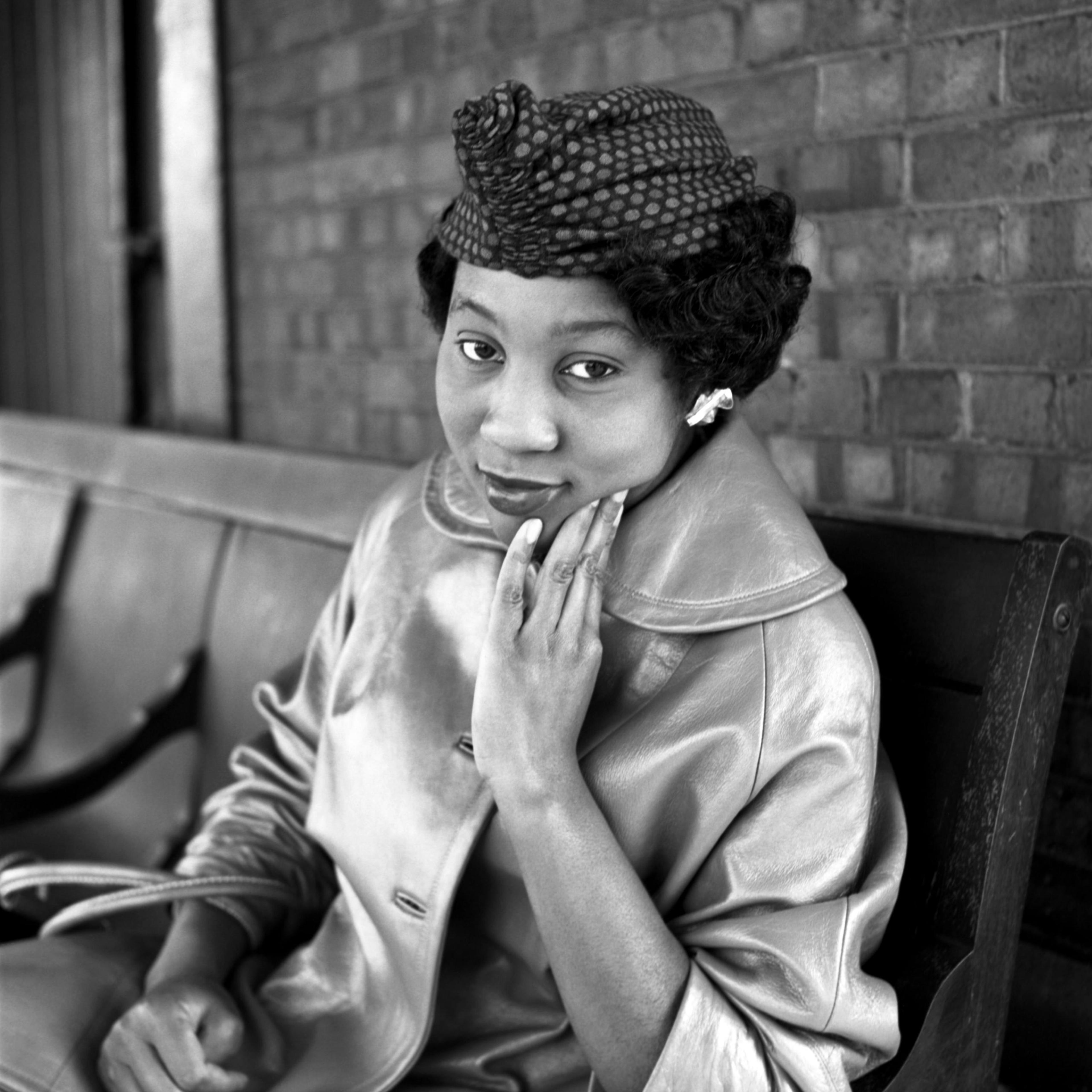A photograph of a sitting woman posing for the camera with her hand resting on her face
