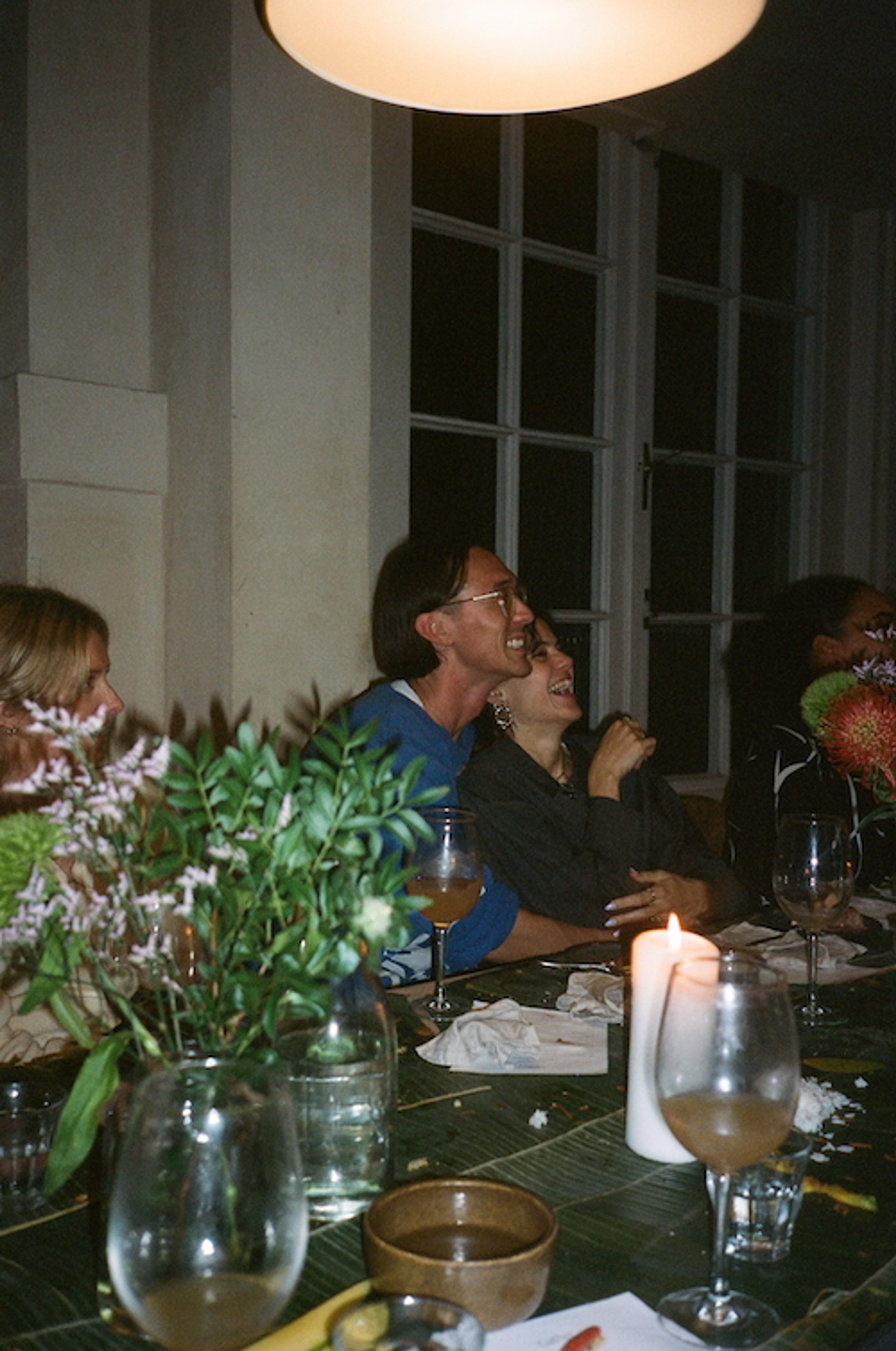 A diverse group of people gathered around the dinner table, engaged in conversation and laughing.