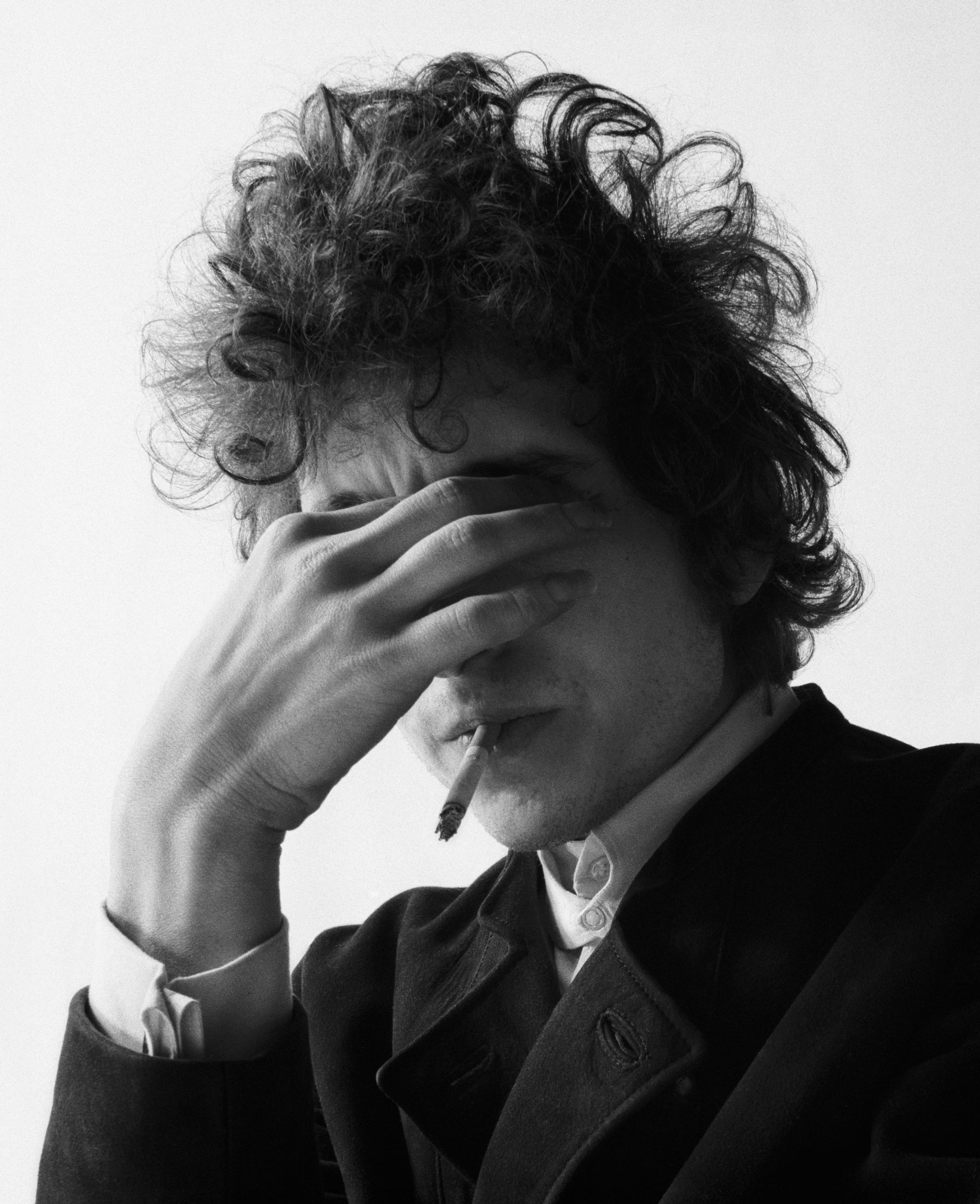 A black and white photograph of Bob Dylan covering his eyes with his hand