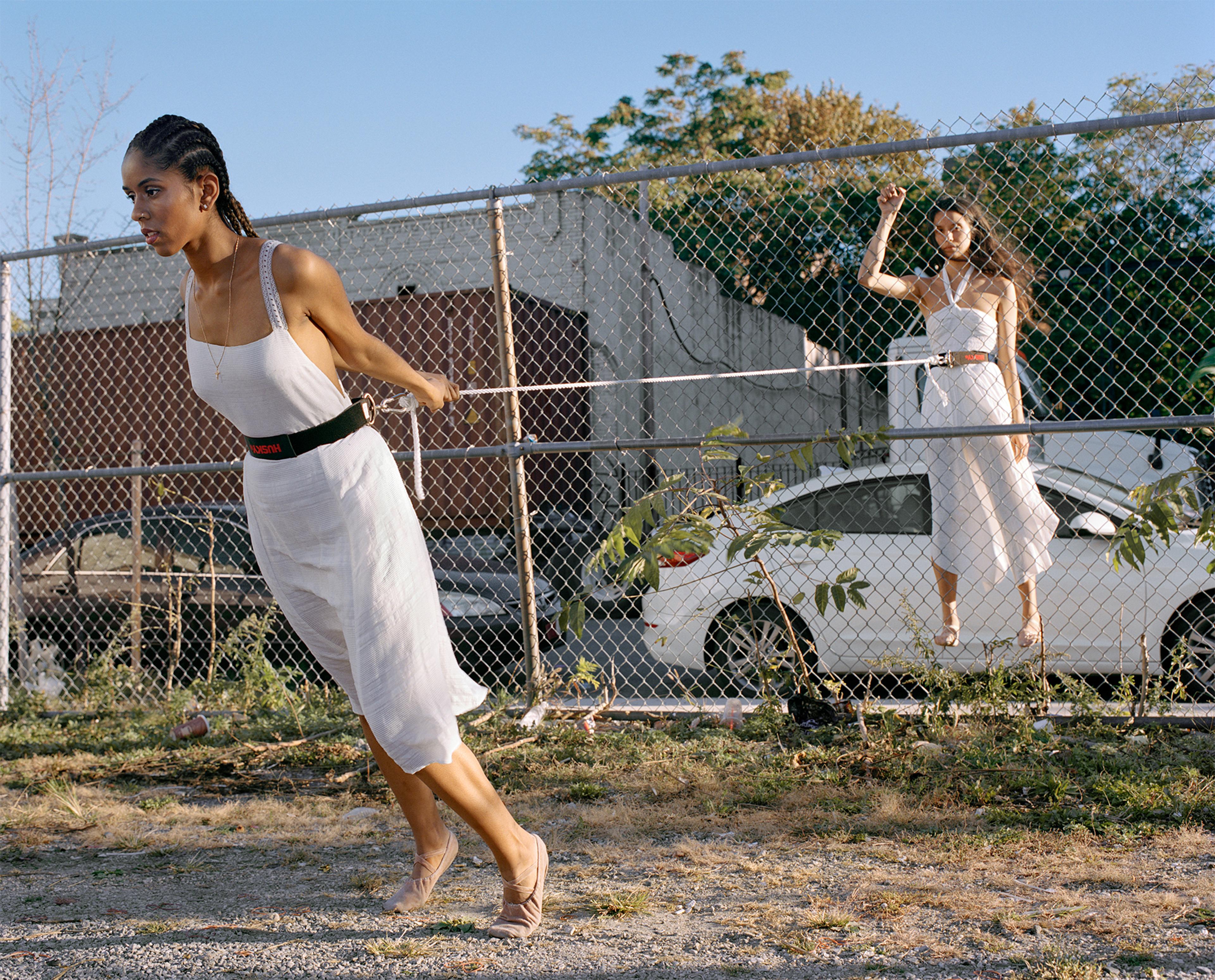 A photograph of two women wearing white clothing at a public park, separated by a chainlink fence