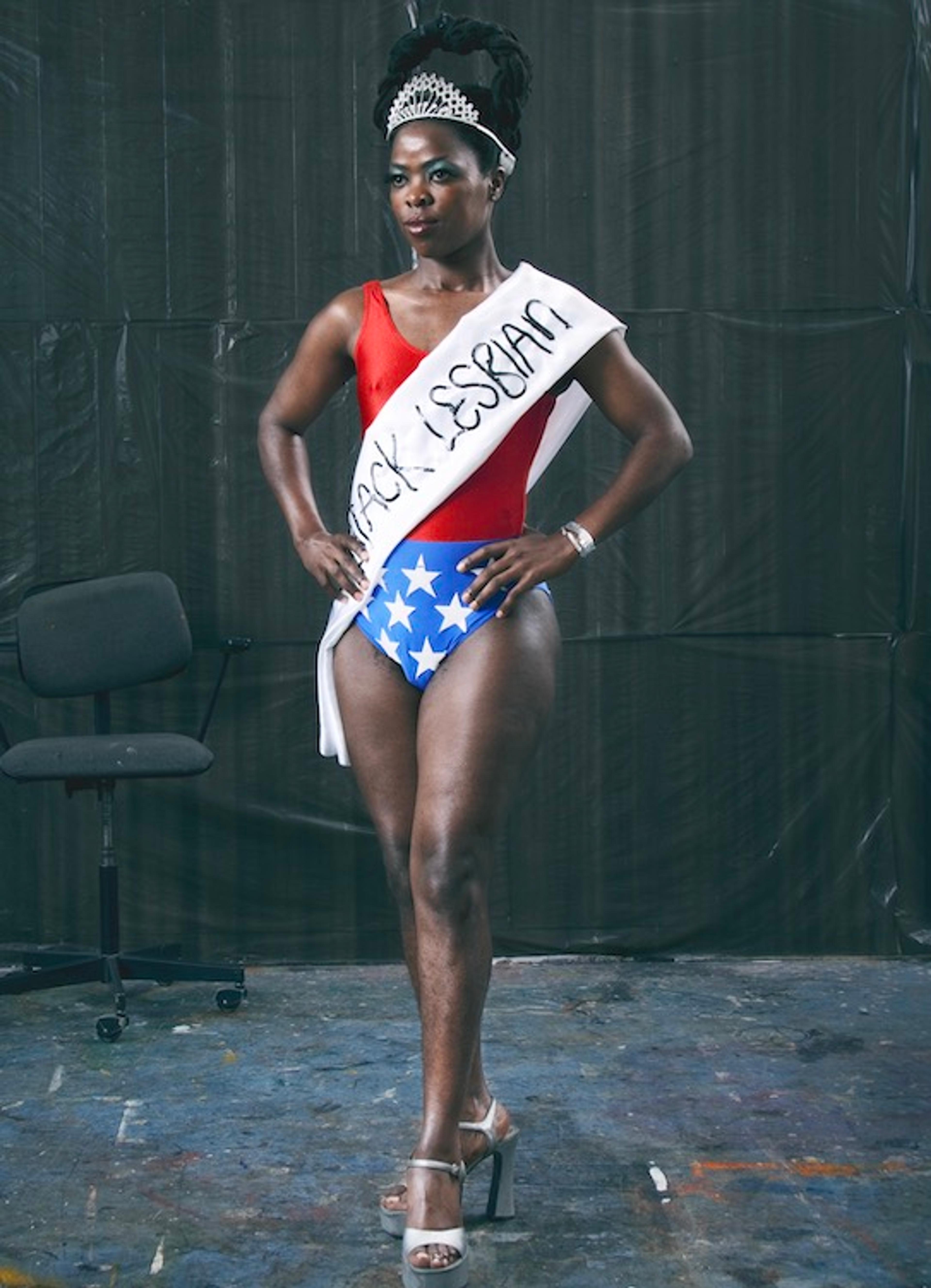 A portrait of a woman wearing a crown, swimsuit, and sash that reads "Miss Black Lesbian"