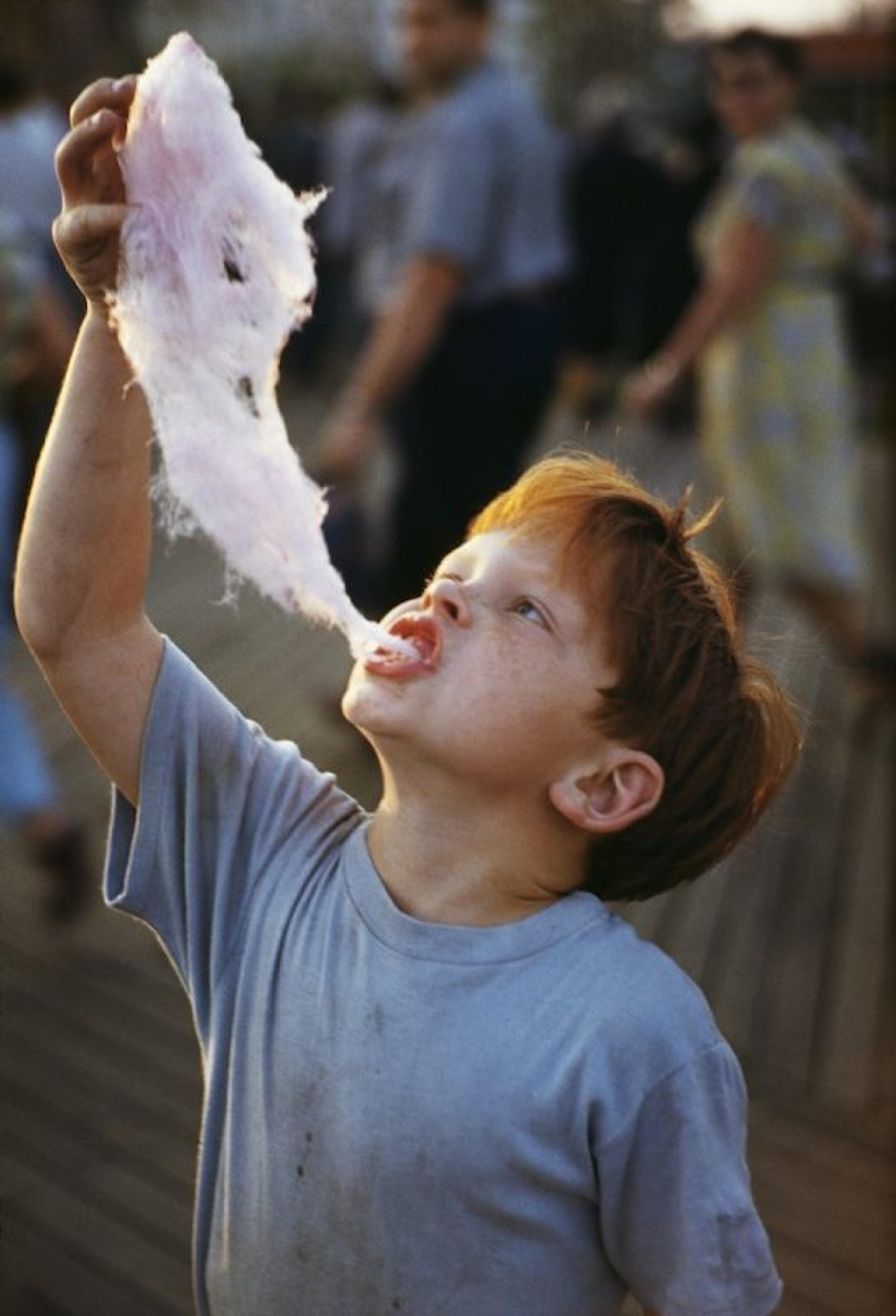 A photograph of a child at a festival dangling cotton candy above their head to eat it