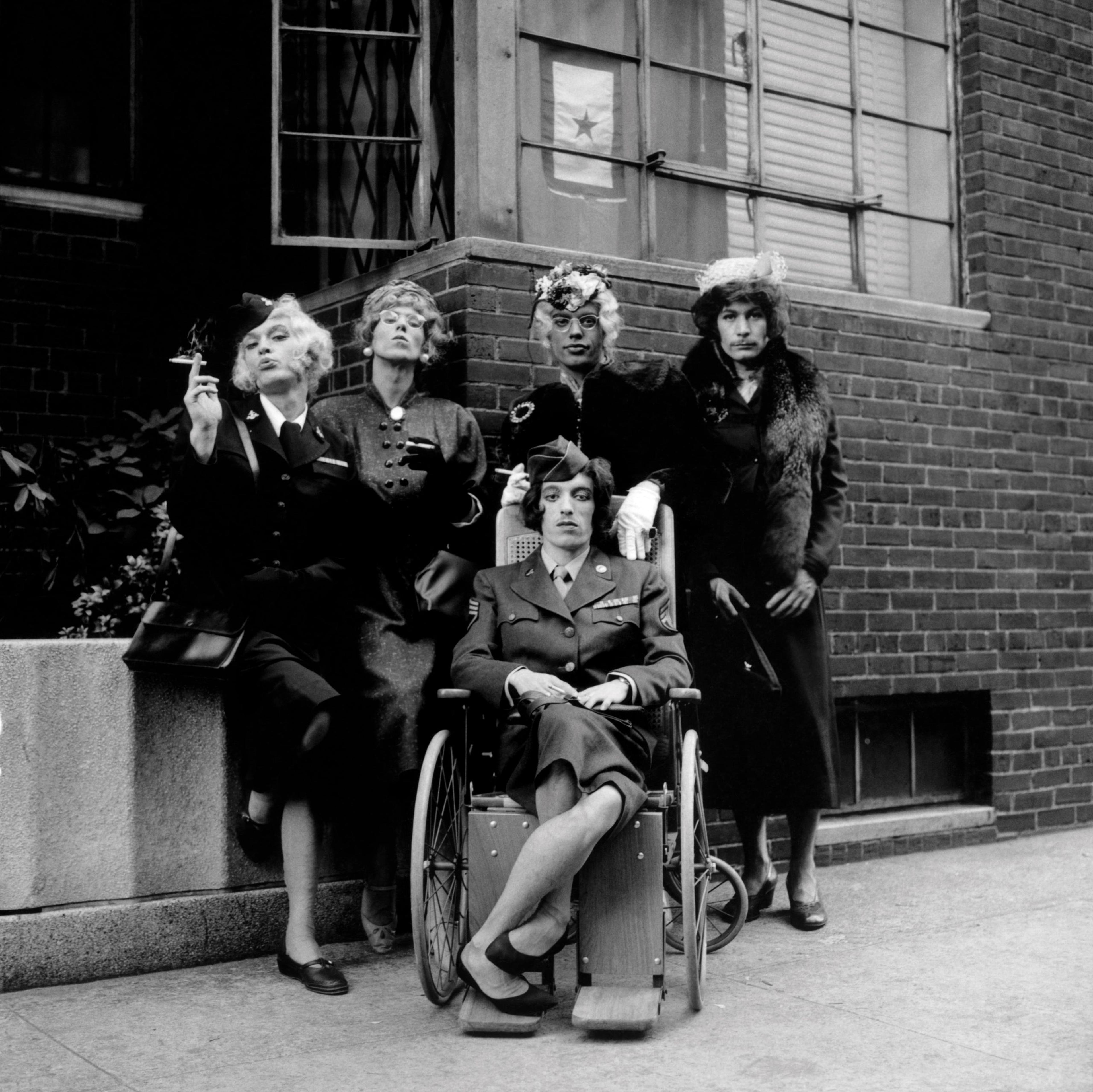 A black-and-white photograph of a group of men in drag on a city street