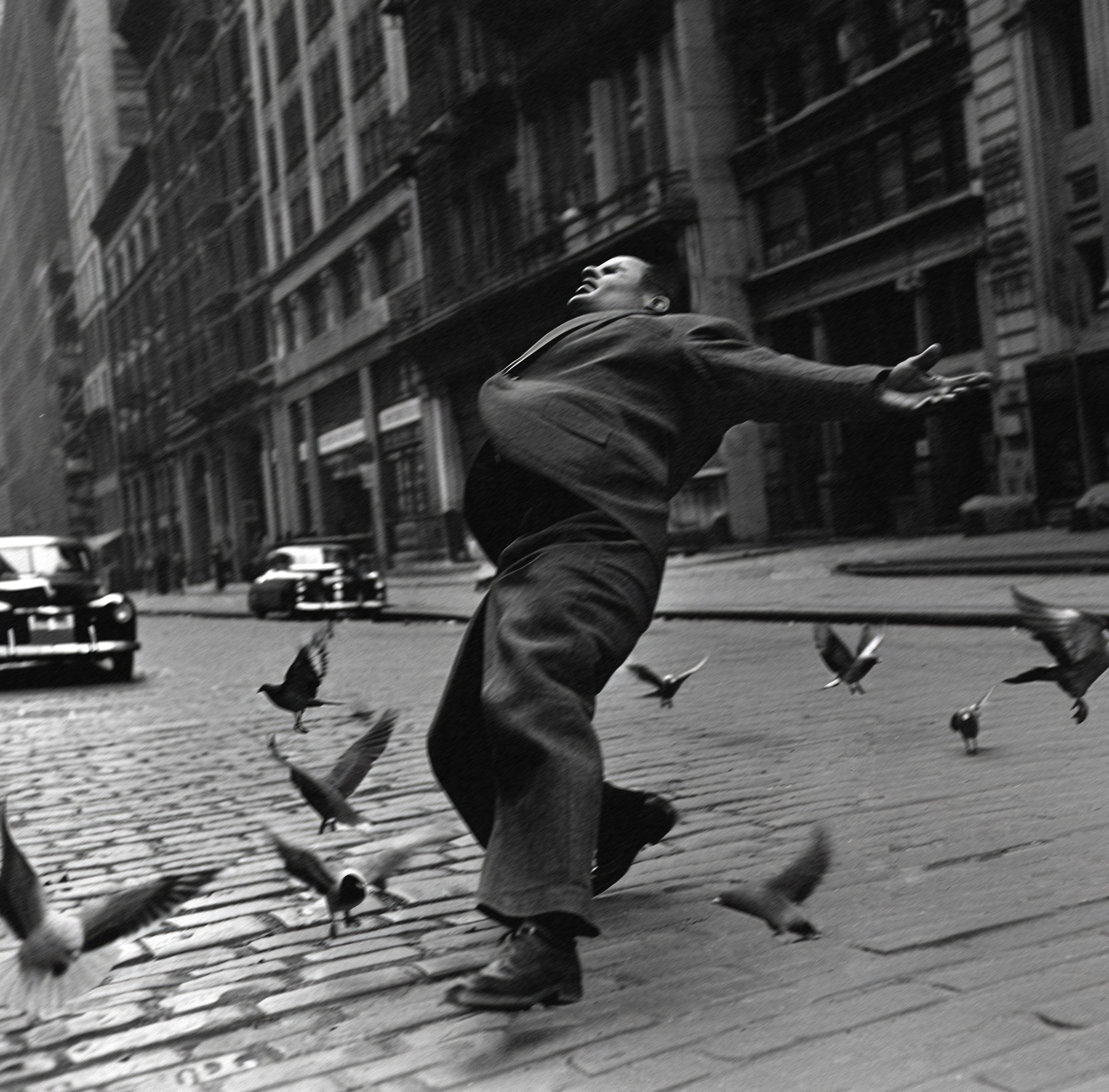 B/w image of a man on a street surrounded by birds and city buildings while slipping