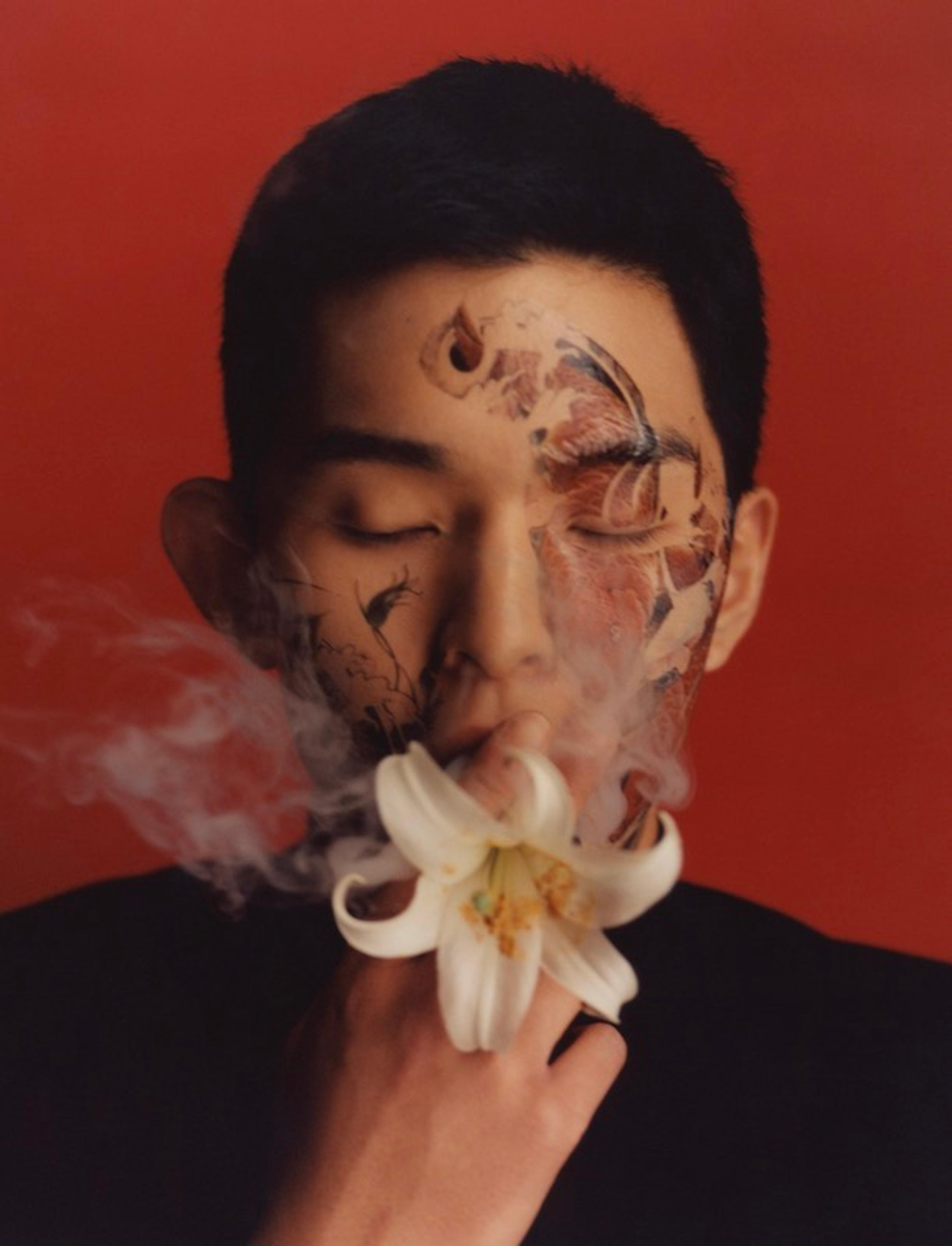 A close-up portrait of a man smoking a flower as if it were a cigarette