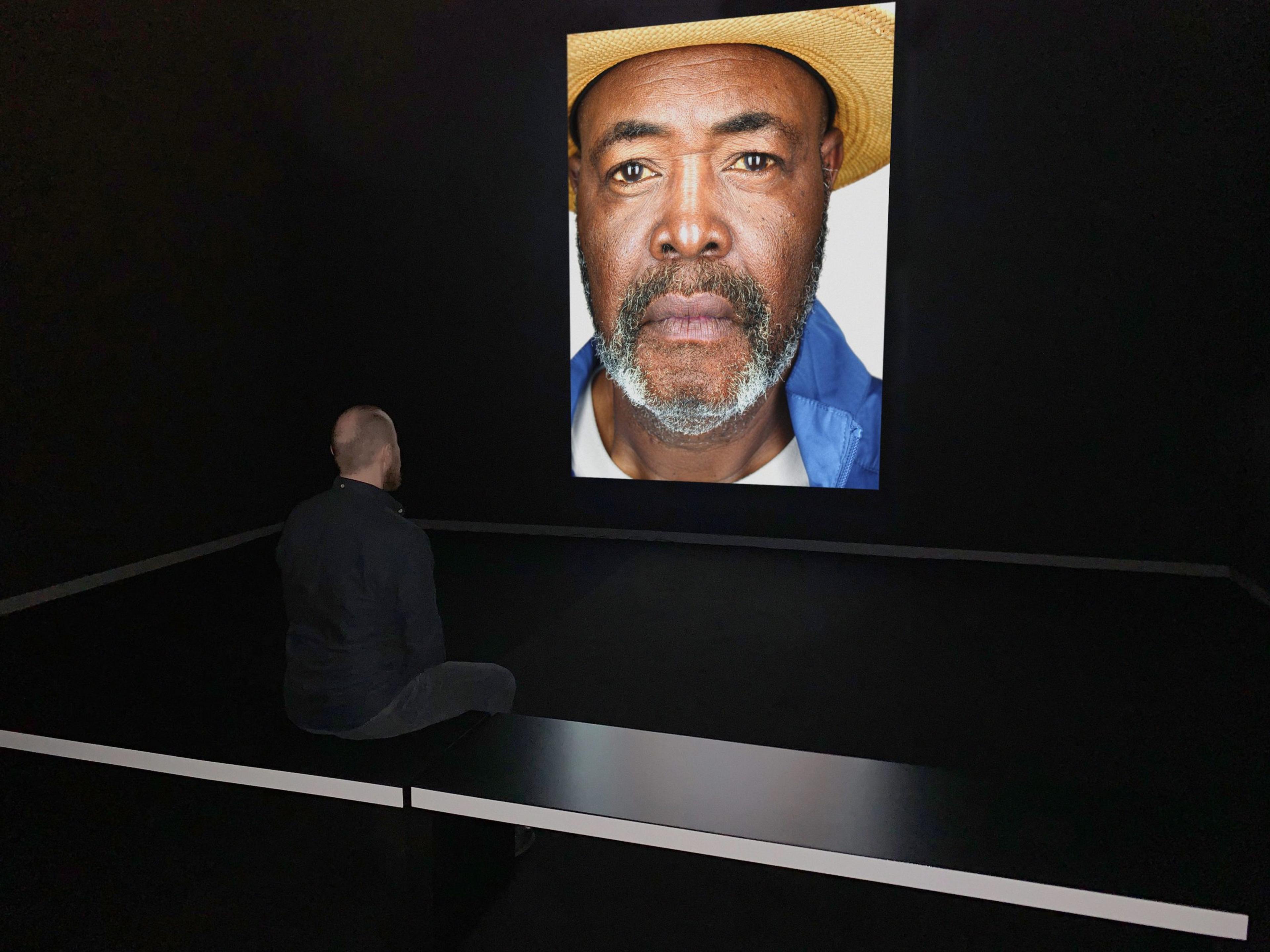 An observer looking at at an image projected in a dark room of a portrait of a man wearing a straw hat