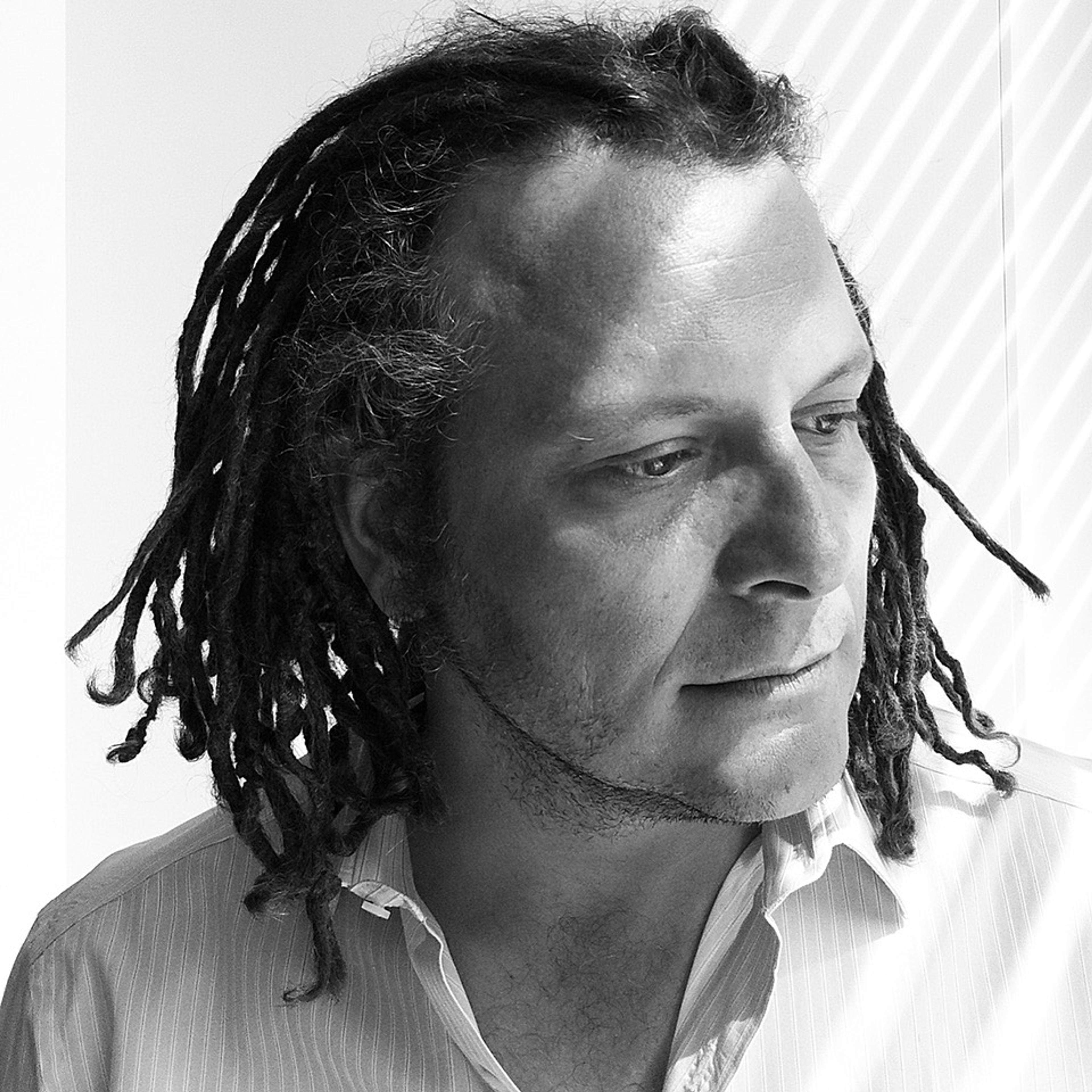 A black and white photograph of a man with short dreadlocks wearing a dress shirt