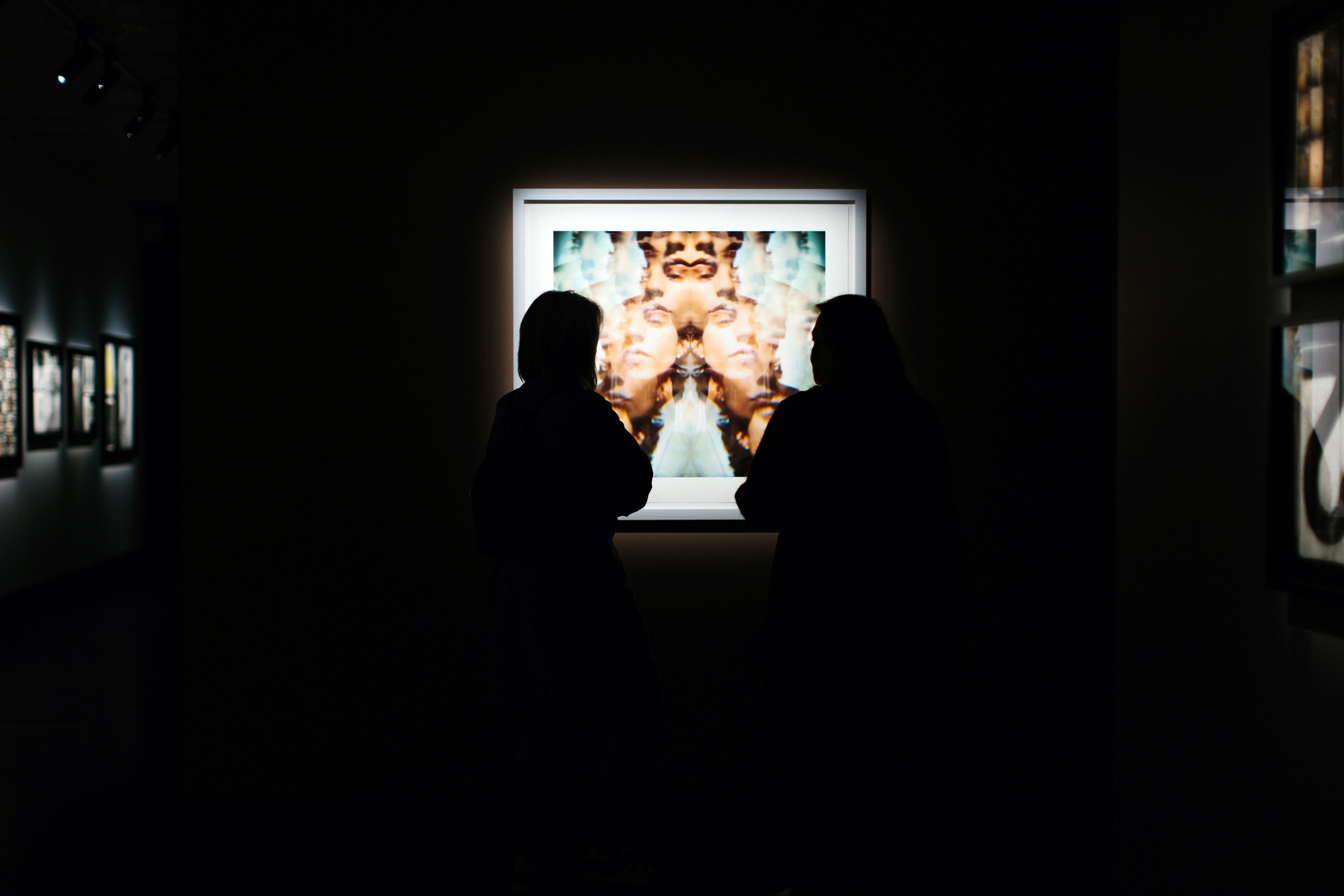 Two people stand in front of a framed photograph in a dark room