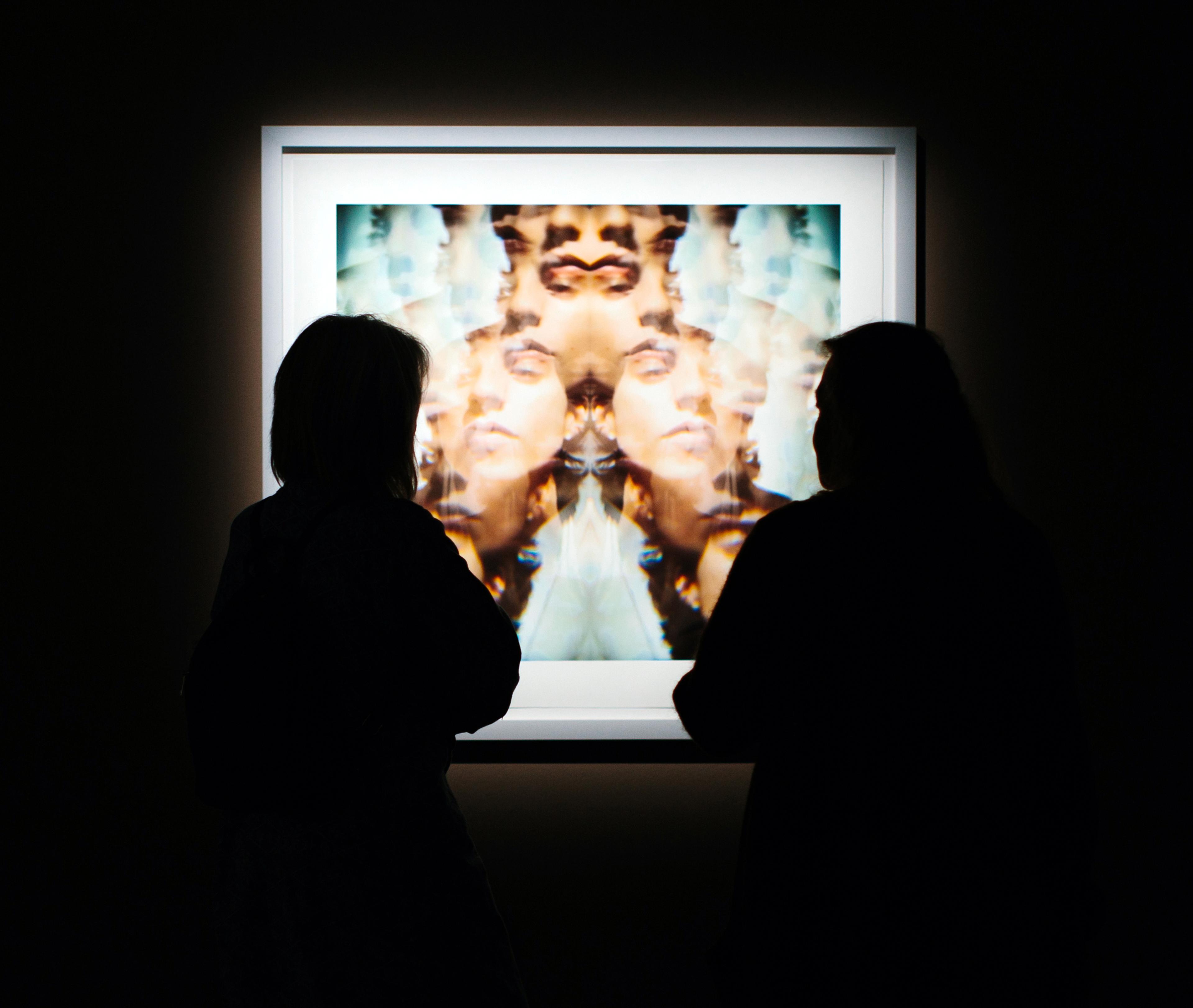 Two people stand in front of a framed photograph in a dark room