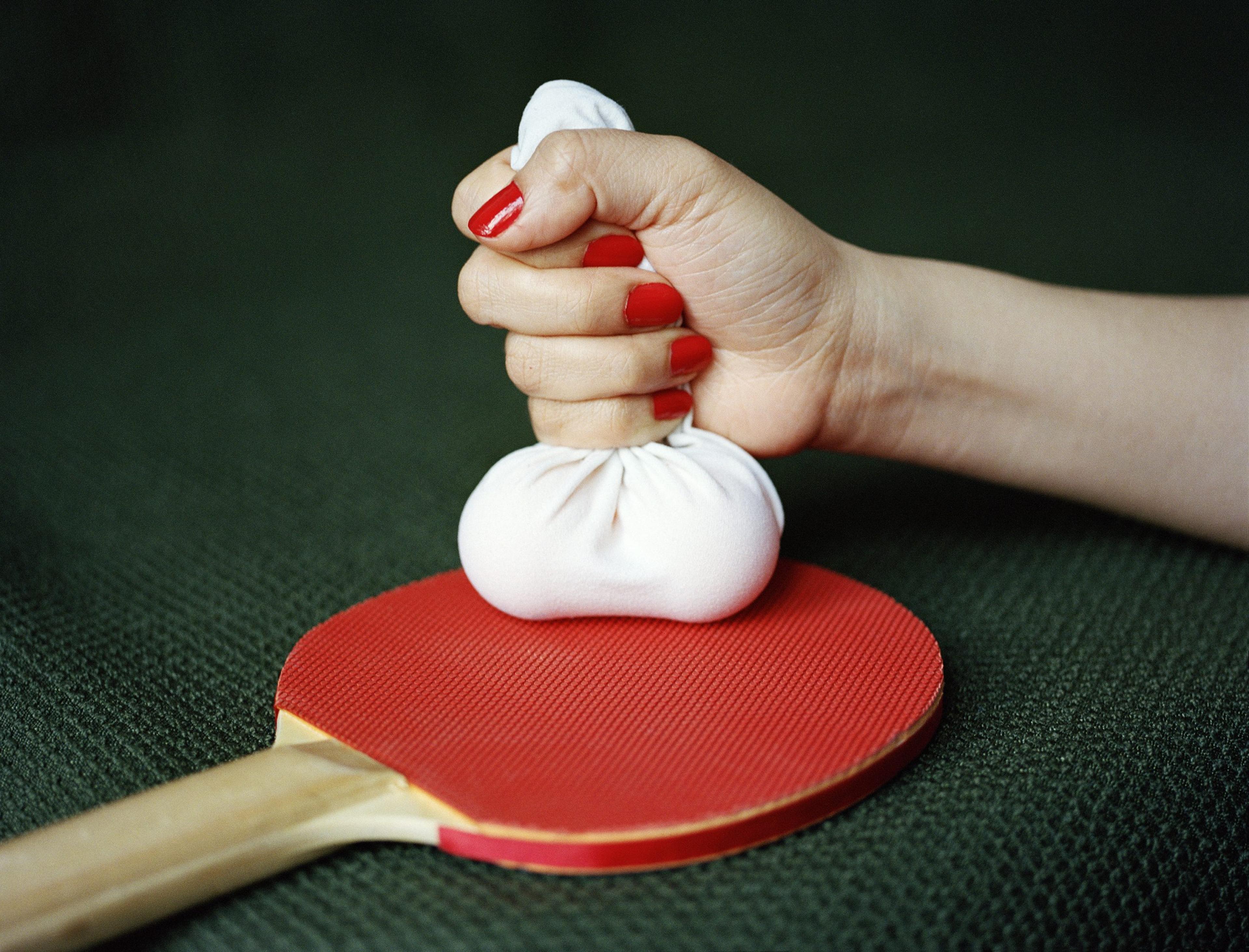 A photograph of a woman's hand holding a phallic object on top of a red ping-pong paddle